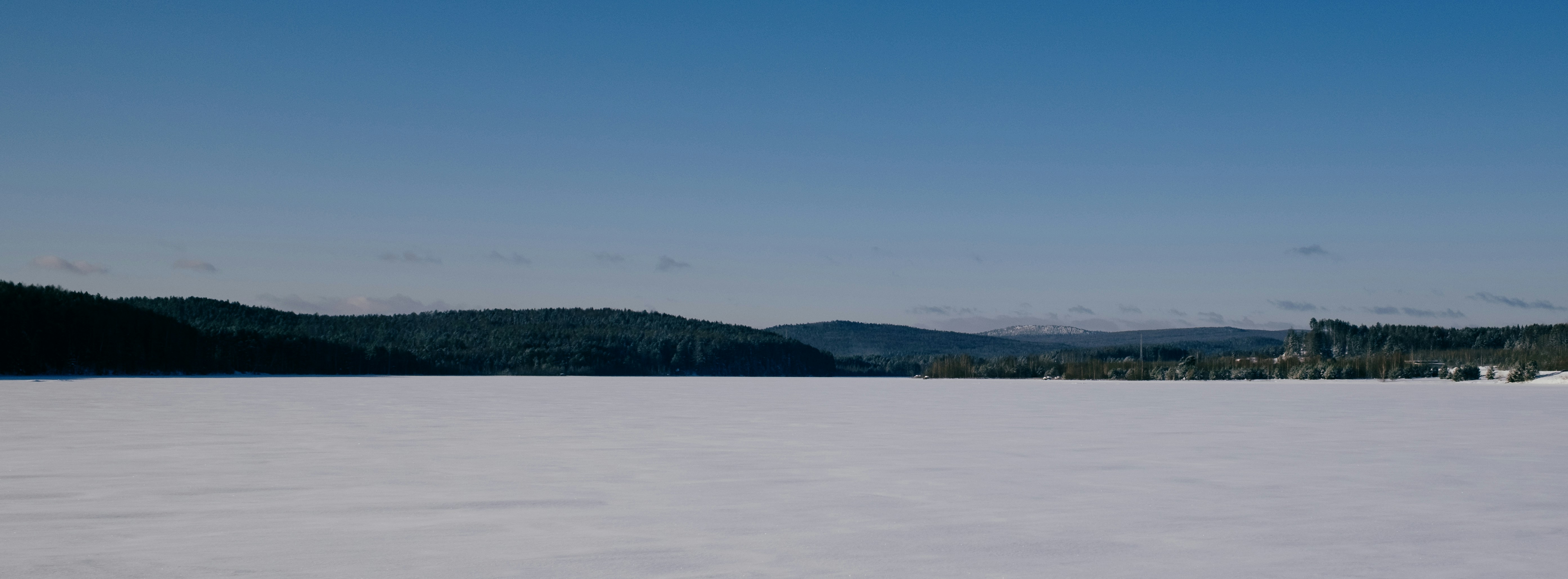 Frozen lake with distant tree-covered hills under blue sky