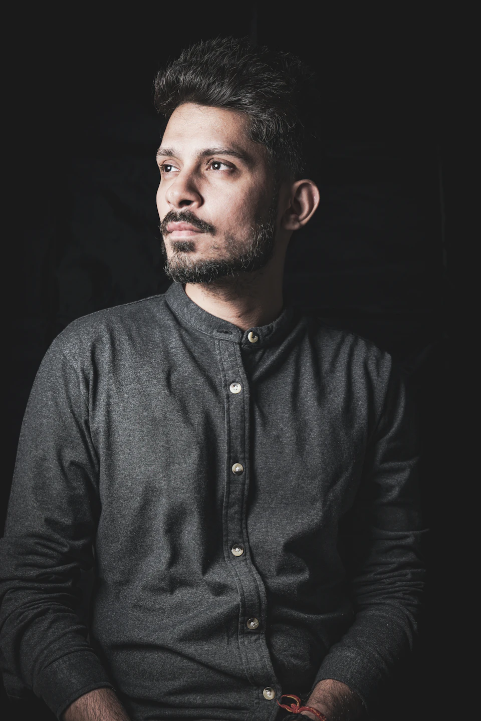 Man sits with beard and mustache, gazing off to the side against dark background