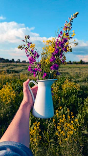 Hand holding a pitcher of wildflowers in a field