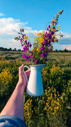 Hand holding a pitcher of wildflowers in a field