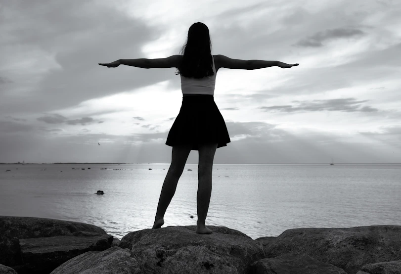 Woman with arms outstretched on rocks by the ocean