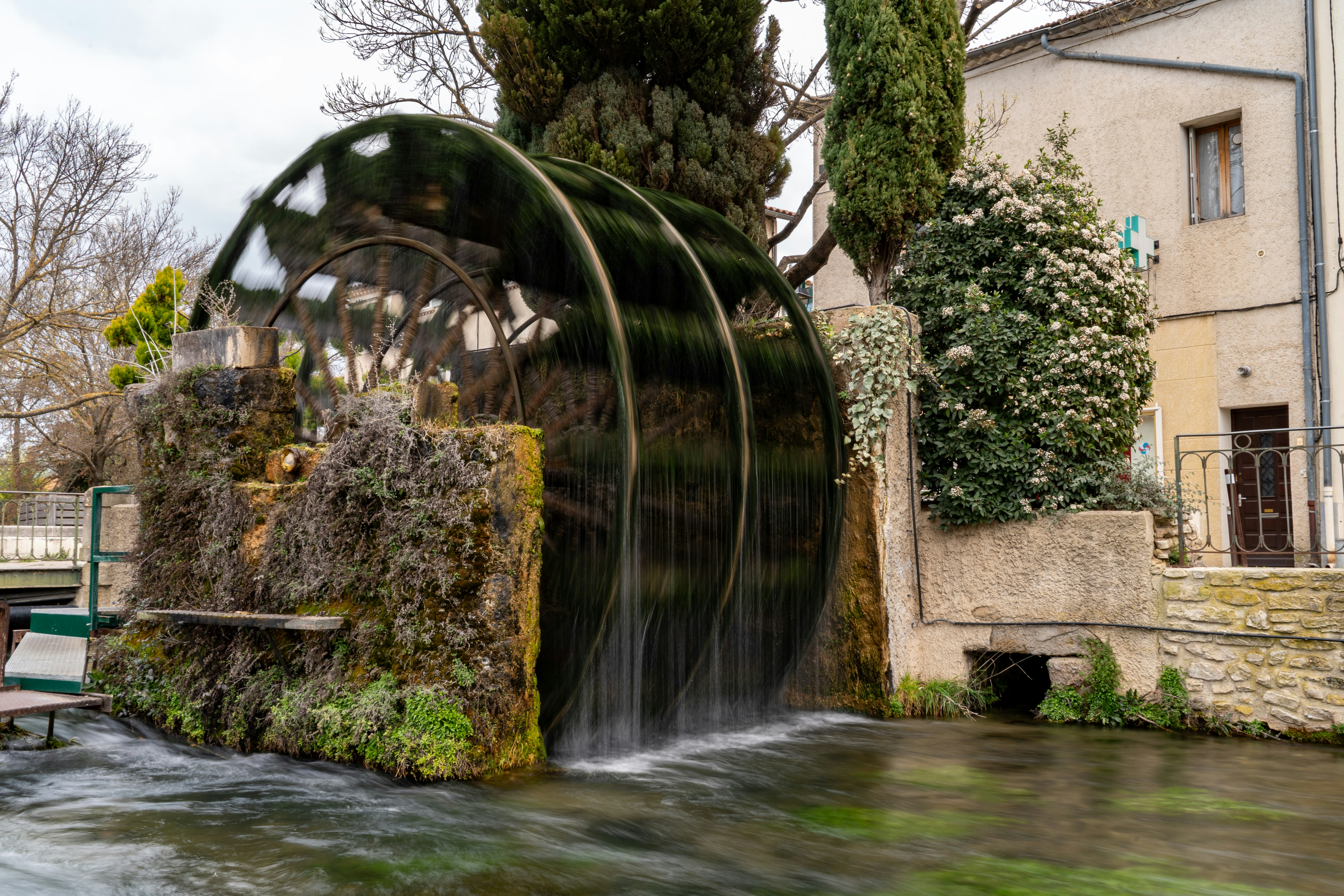 La roue à eau tourne dans un ruisseau près d’un bâtiment.