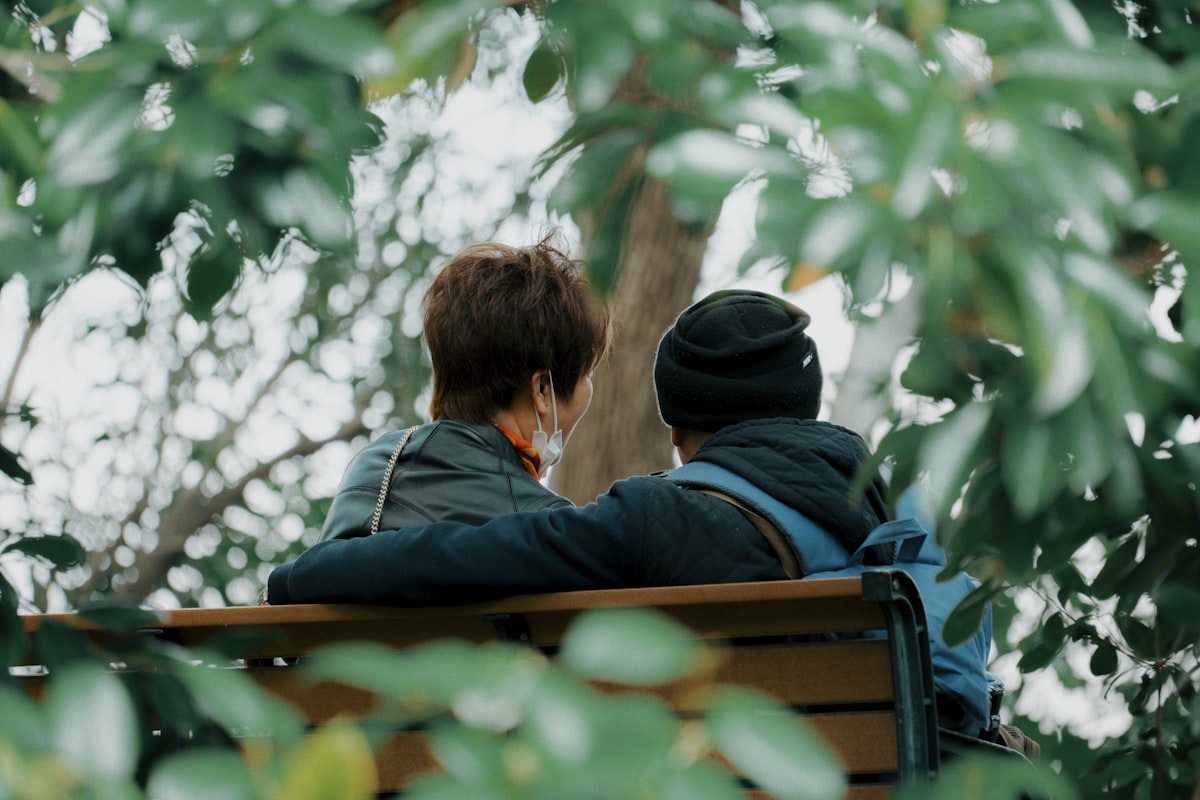 Two people sitting on a park bench surrounded by autumn leaves, quiet companionship