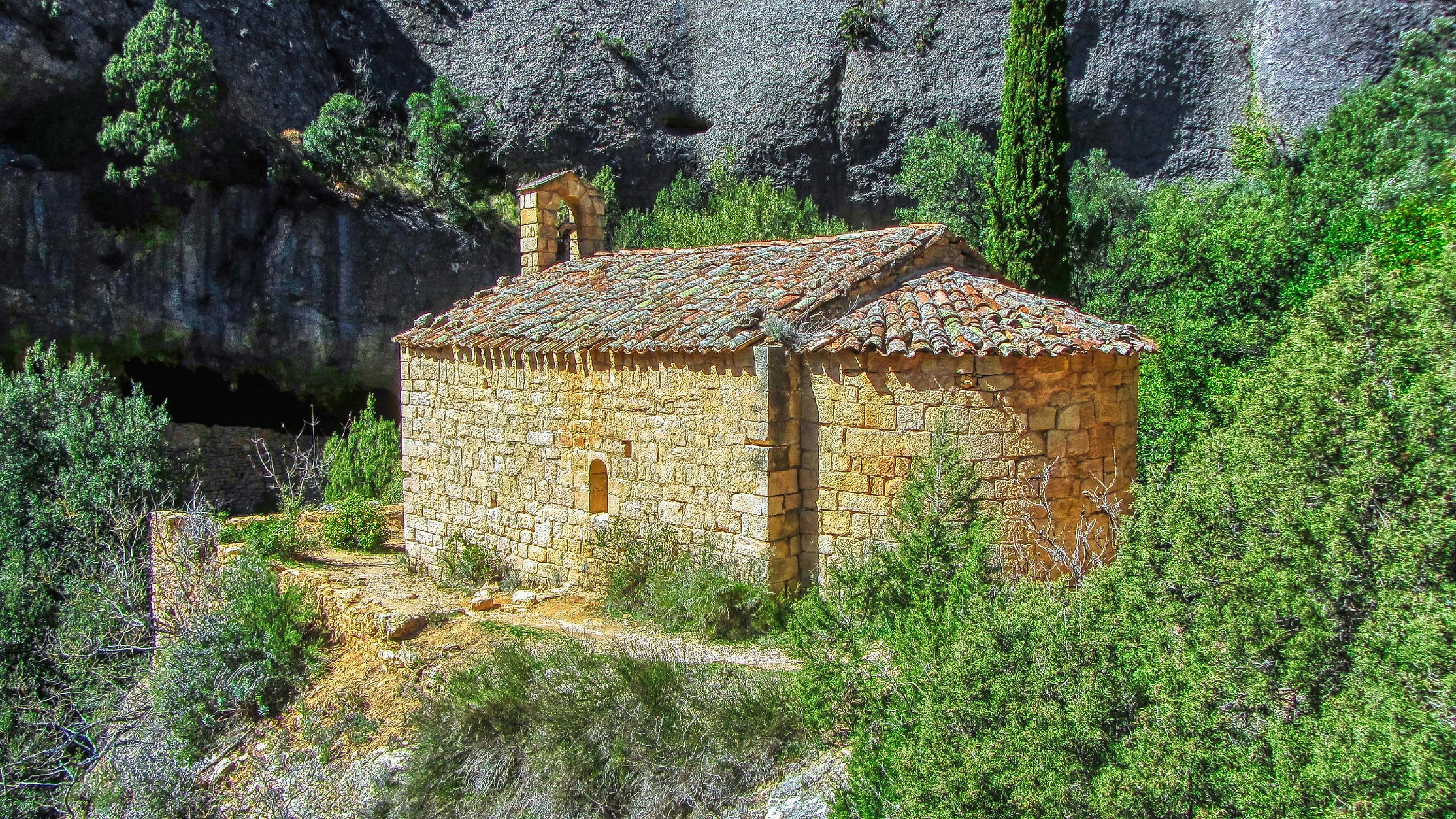 Small stone chapel nestled in a rocky, green landscape.