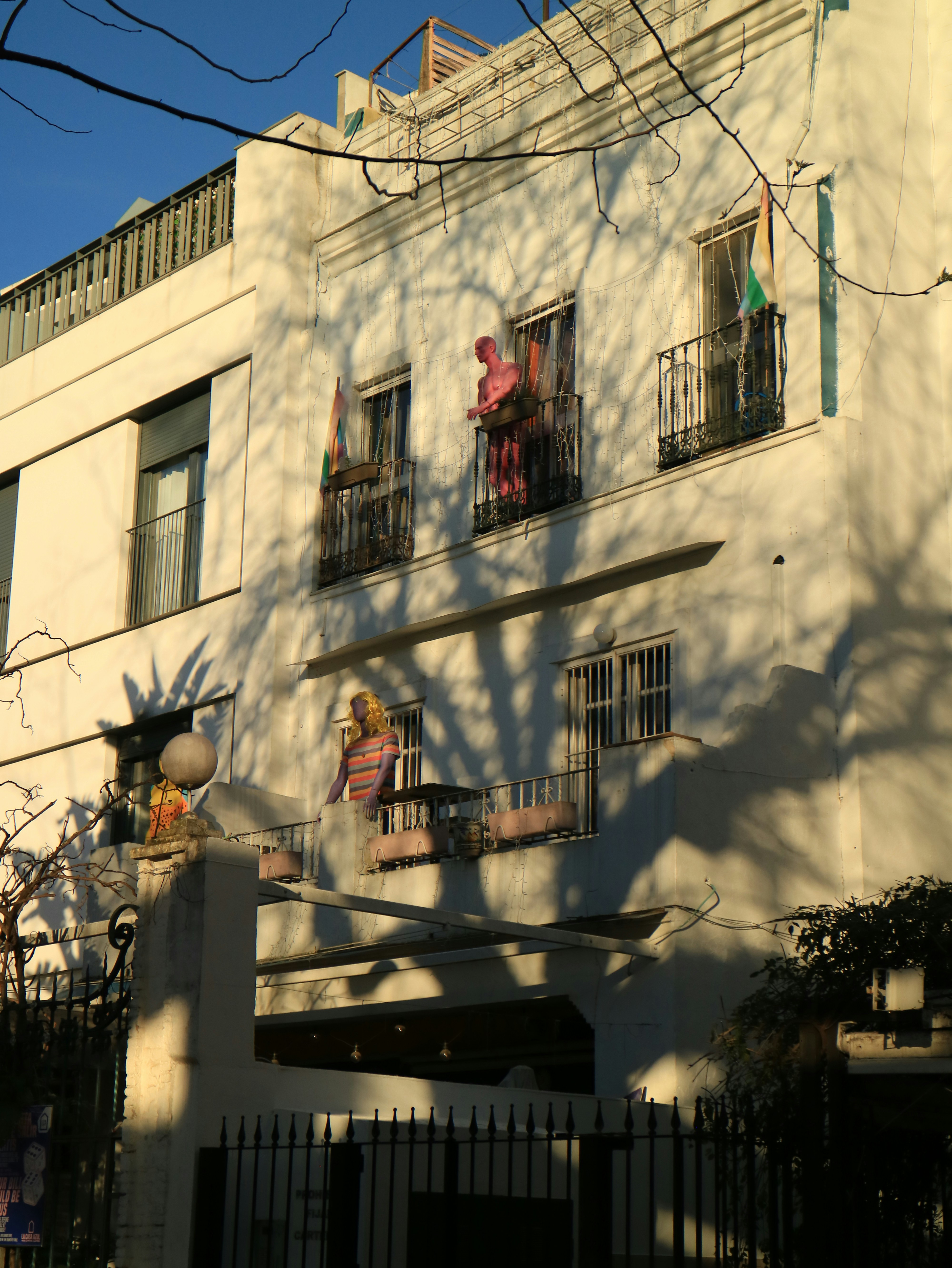 Duas figuras estão em varandas de um prédio branco.