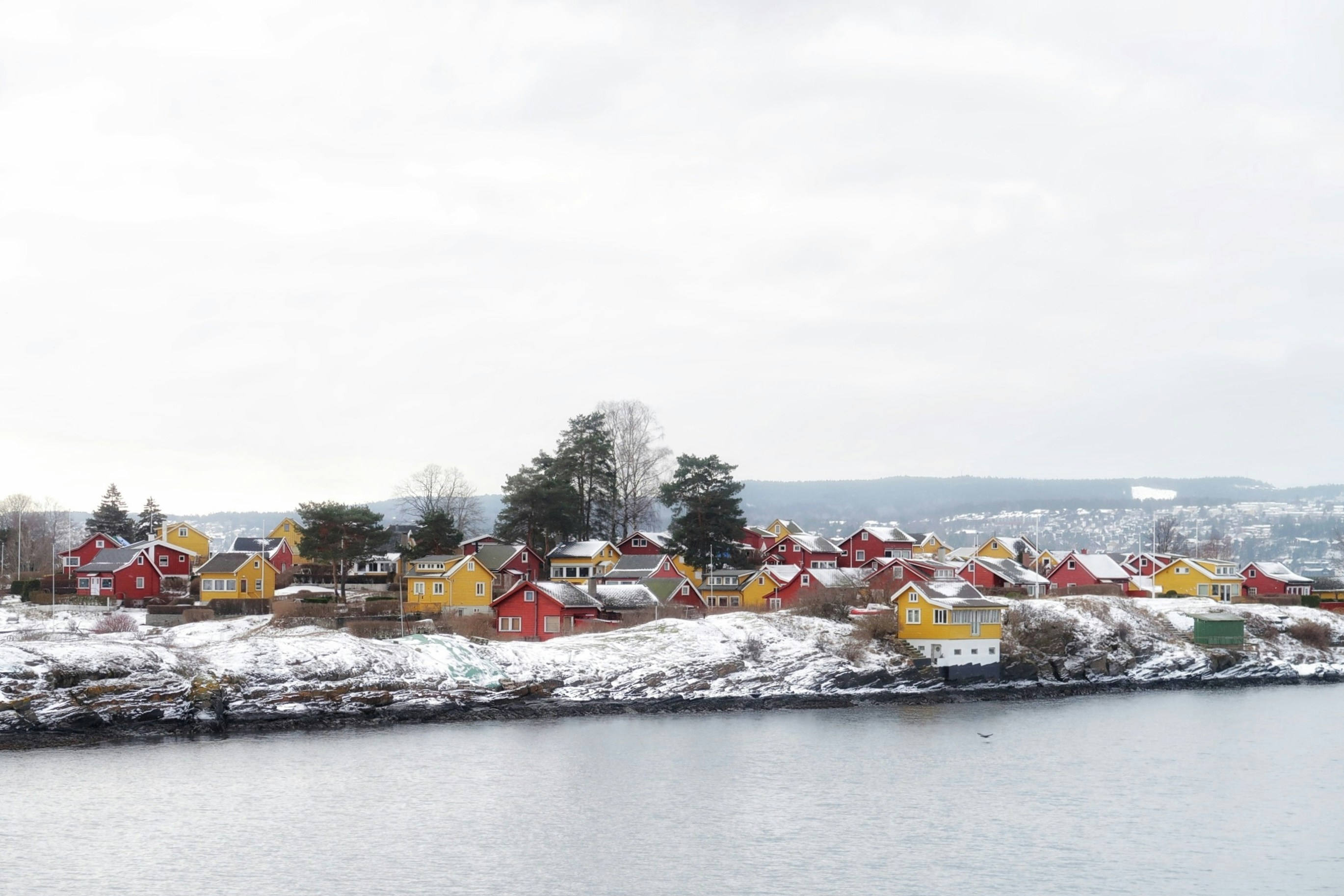 Colorful houses on a snowy island with calm water.
