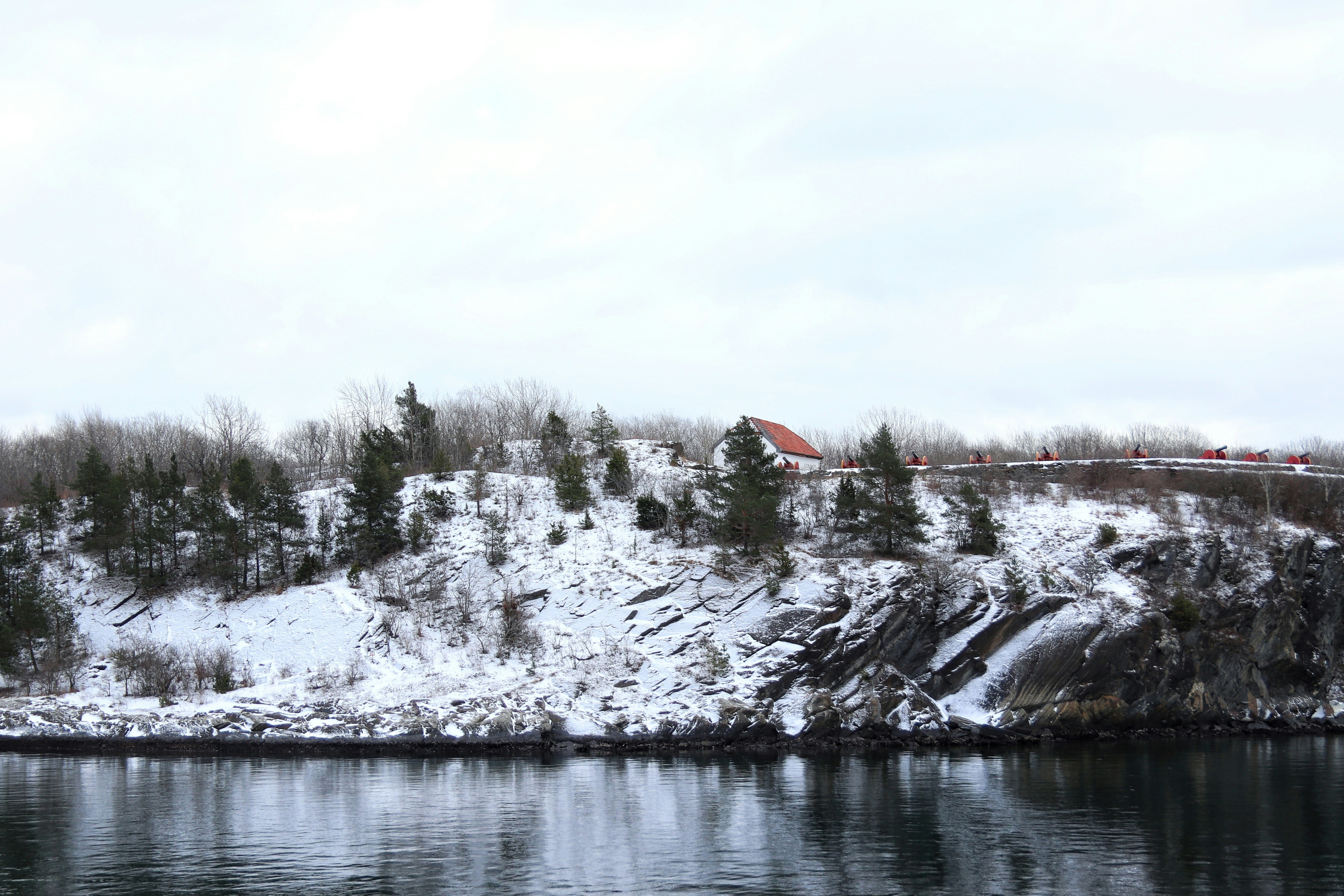 Snow-covered cliff with trees and calm water