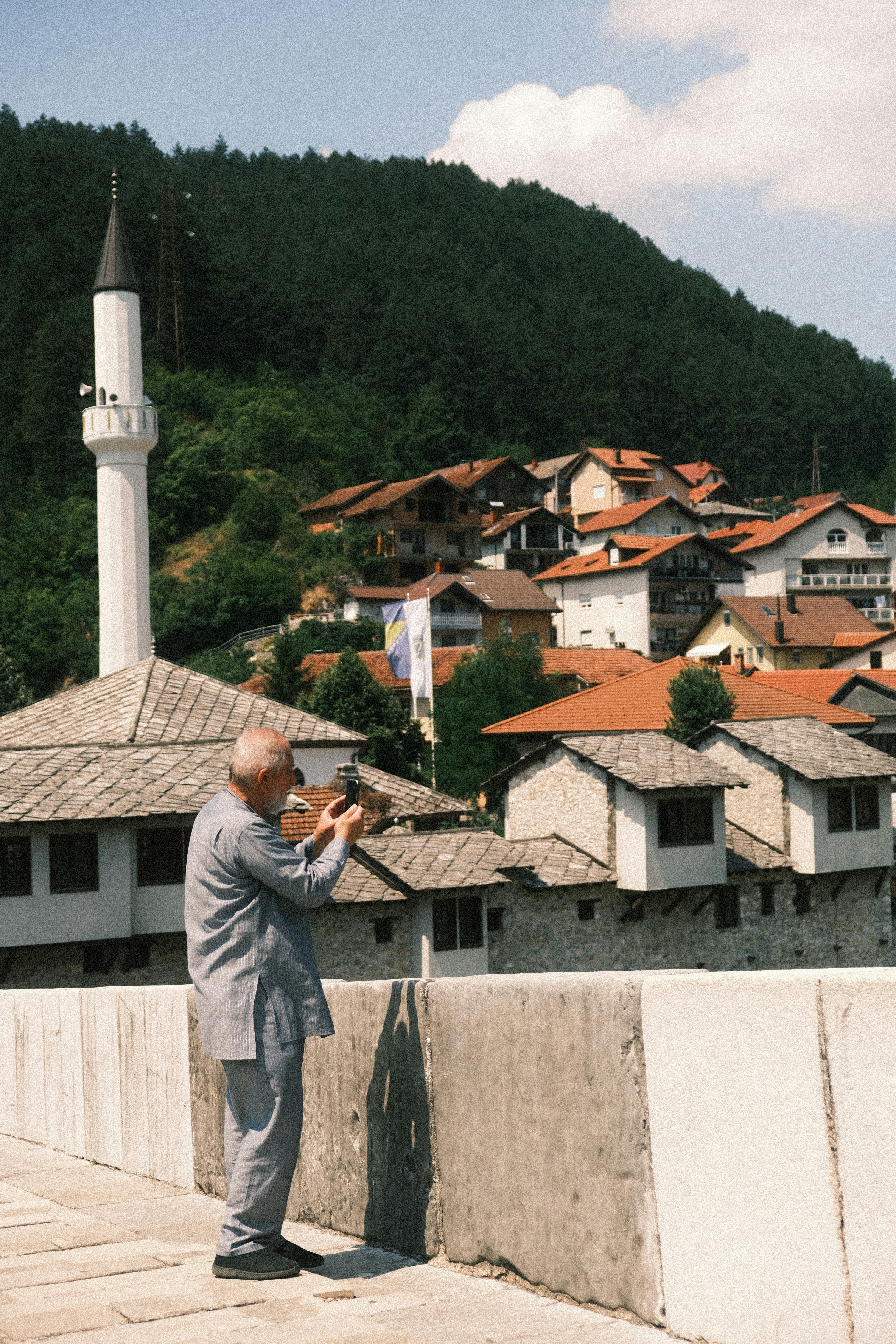 Man photographing buildings with a mosque in the background.