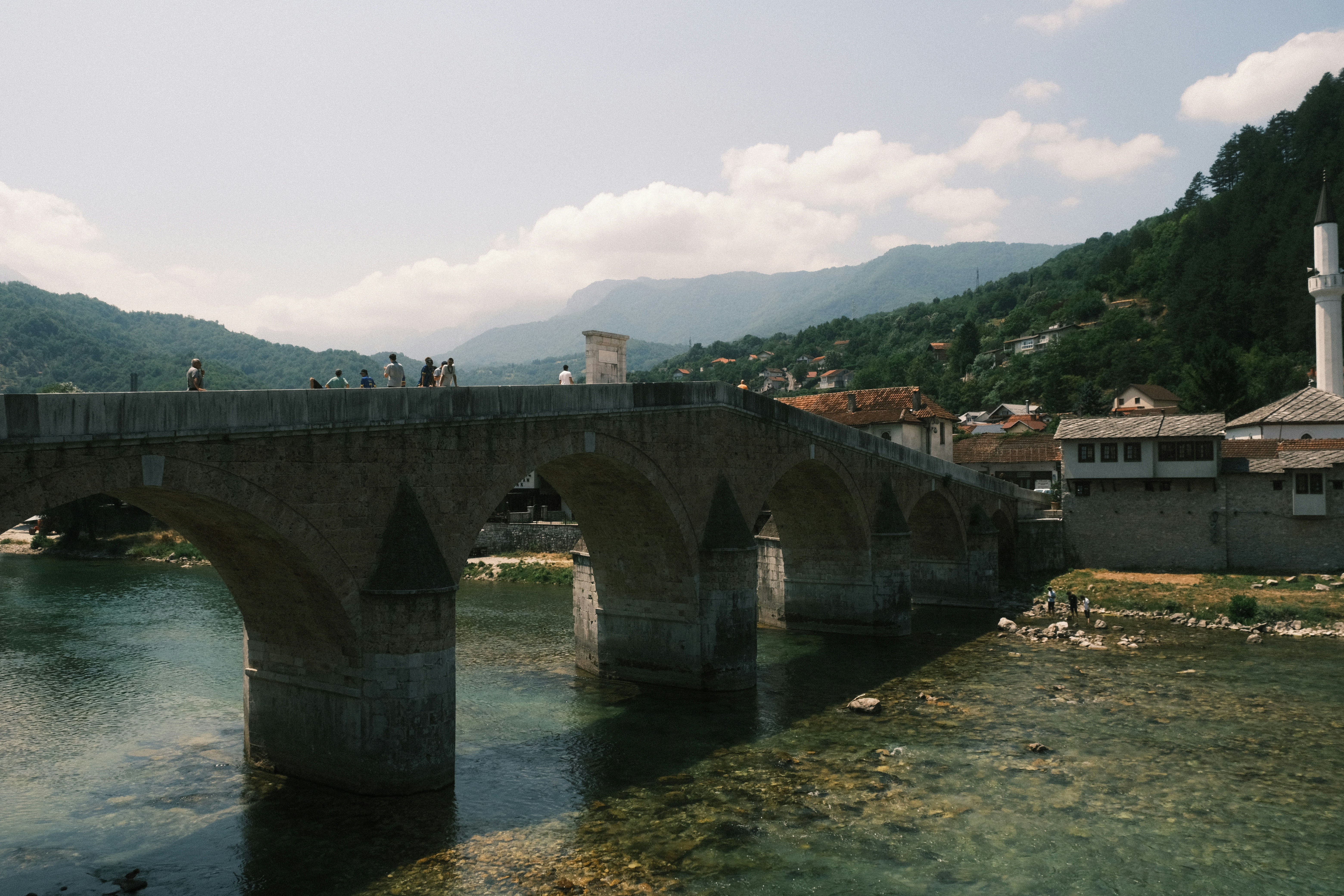 Historic stone bridge over a clear river with mountains.