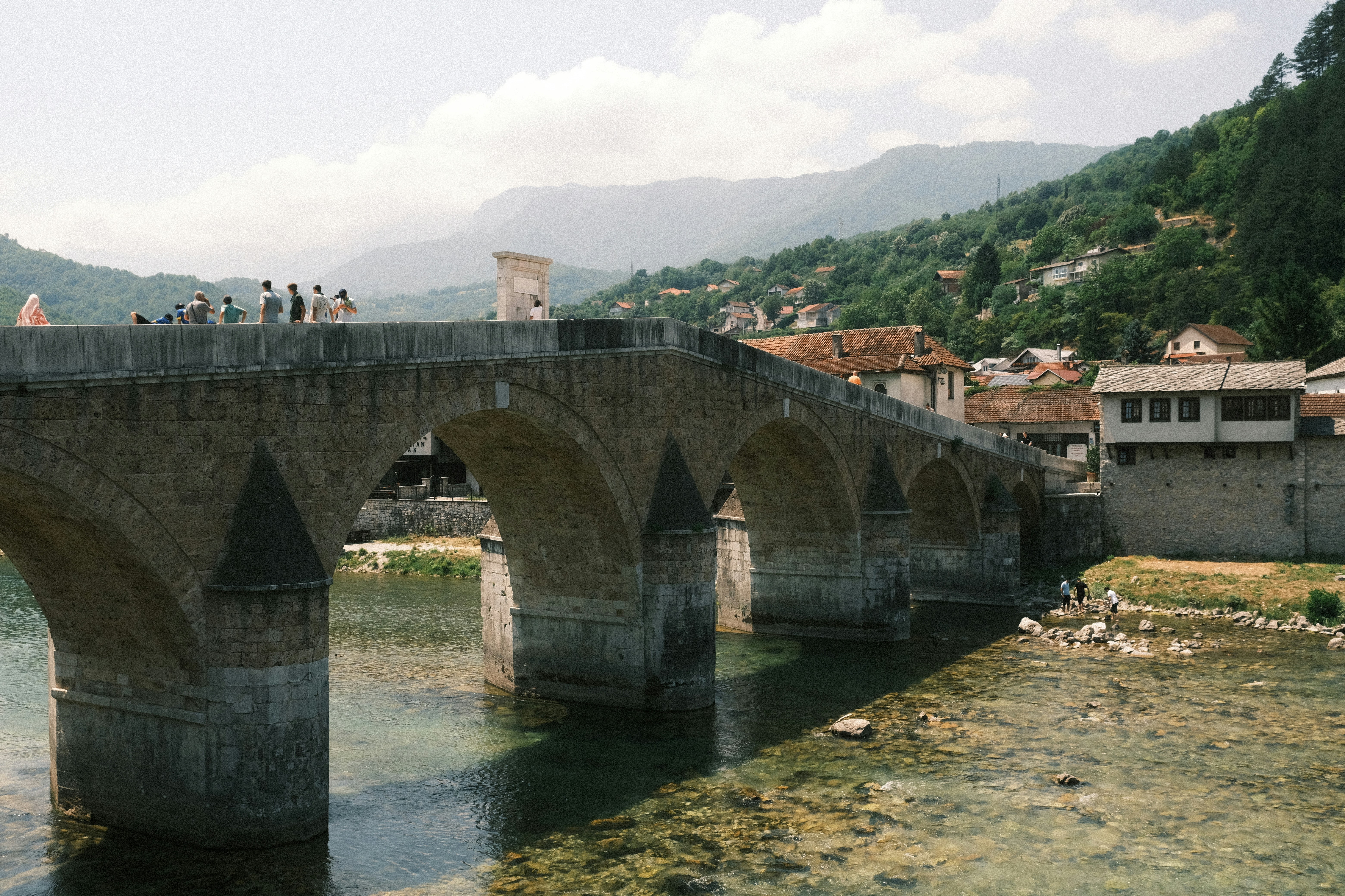 Old stone bridge arches over a clear river with town.