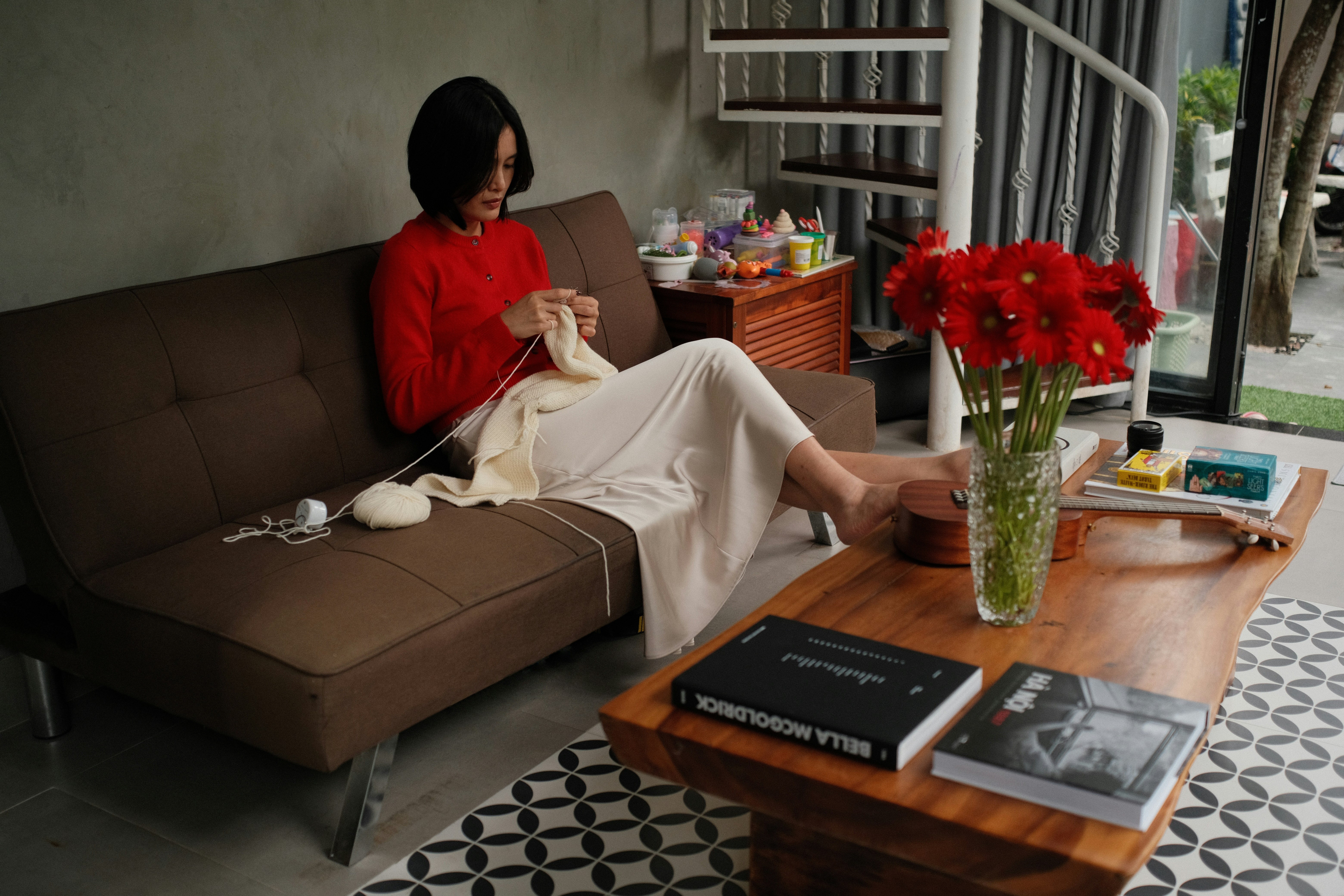 Woman knitting on a sofa with flowers on table