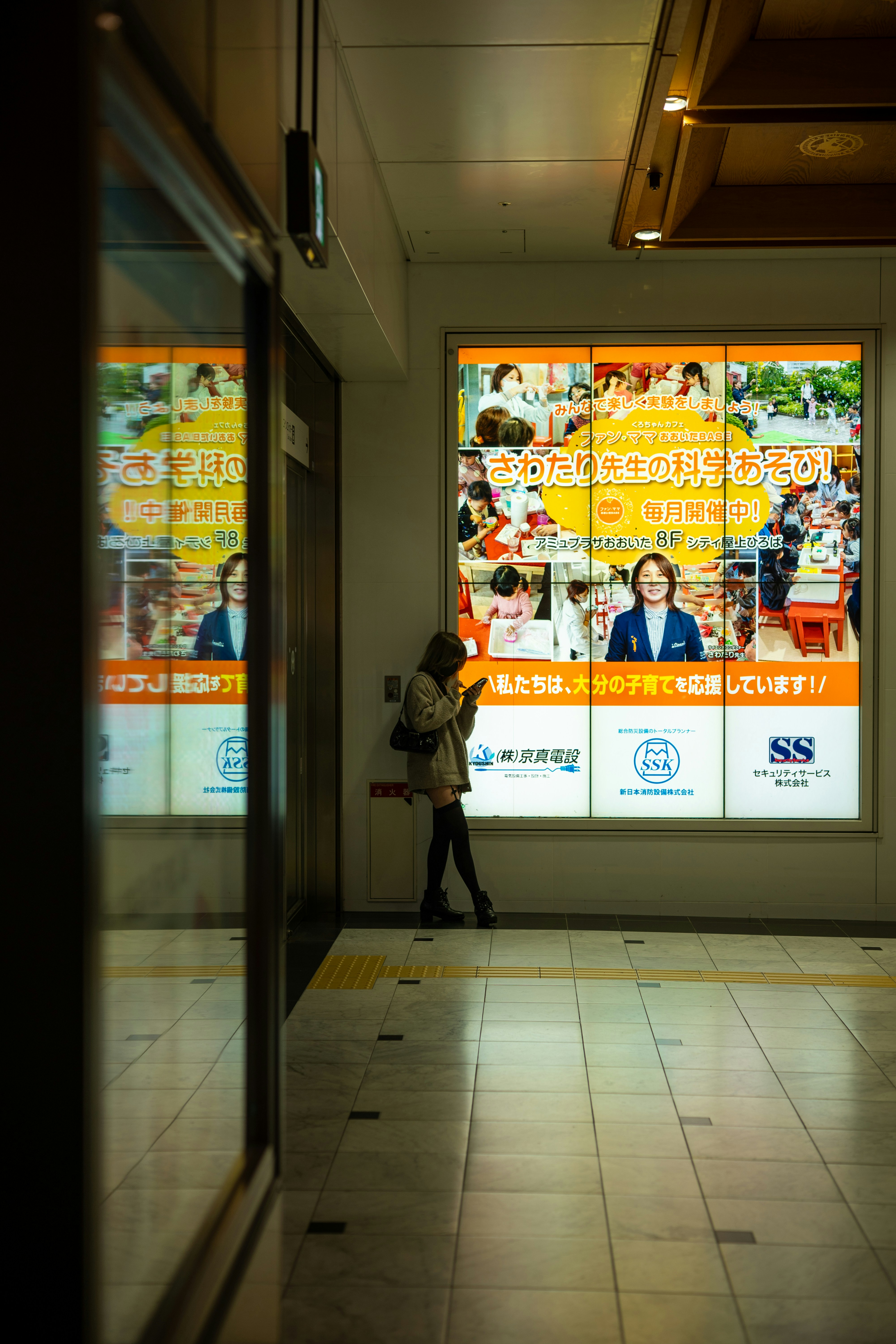 Femme regardant son téléphone près d’une grande publicité illuminée.