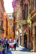 People walk down a narrow street with buildings and restaurants.