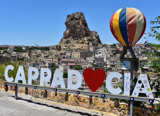 Cappadocia sign with hot air balloon and rock formations.