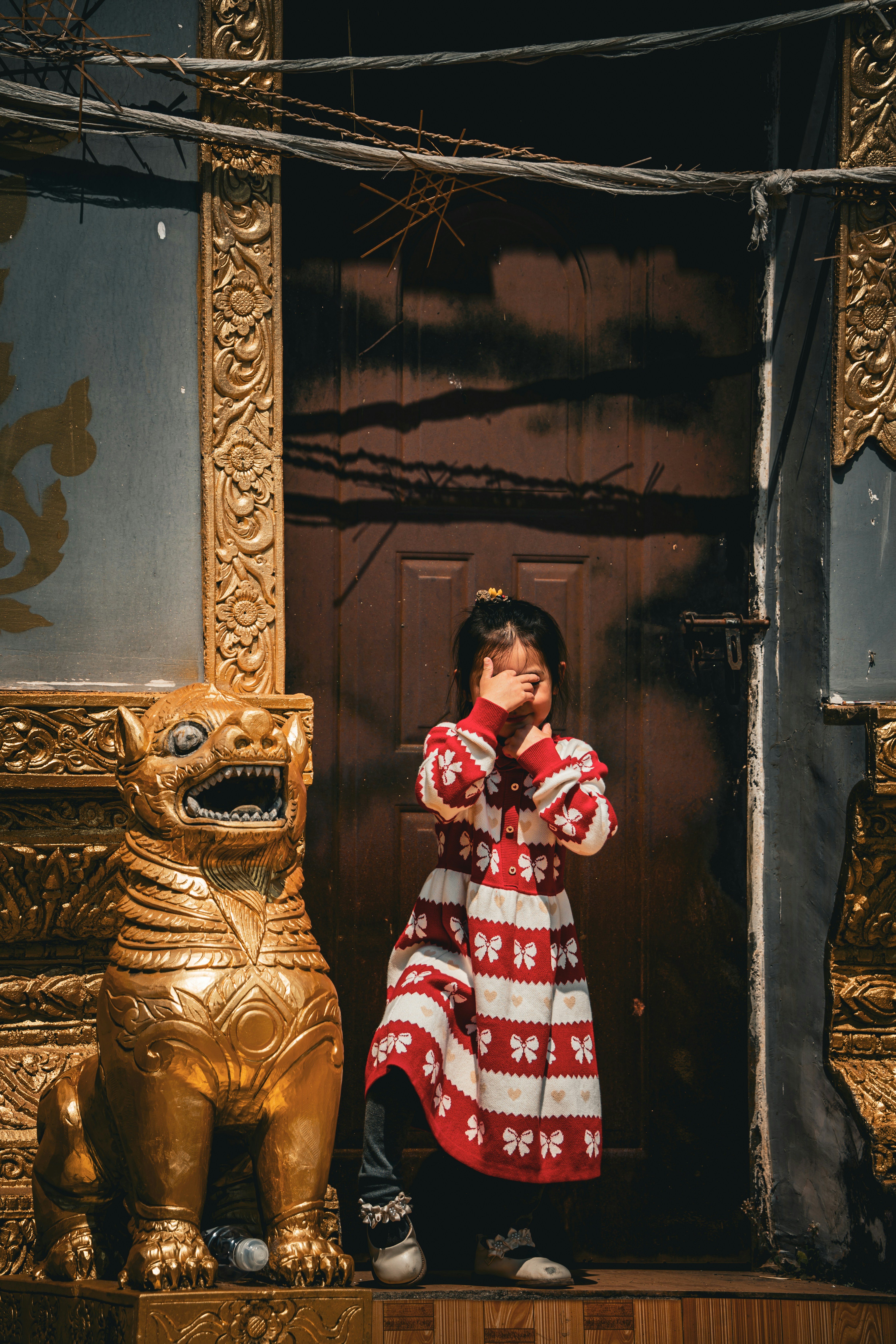 Young girl in red and white dress covers her eyes