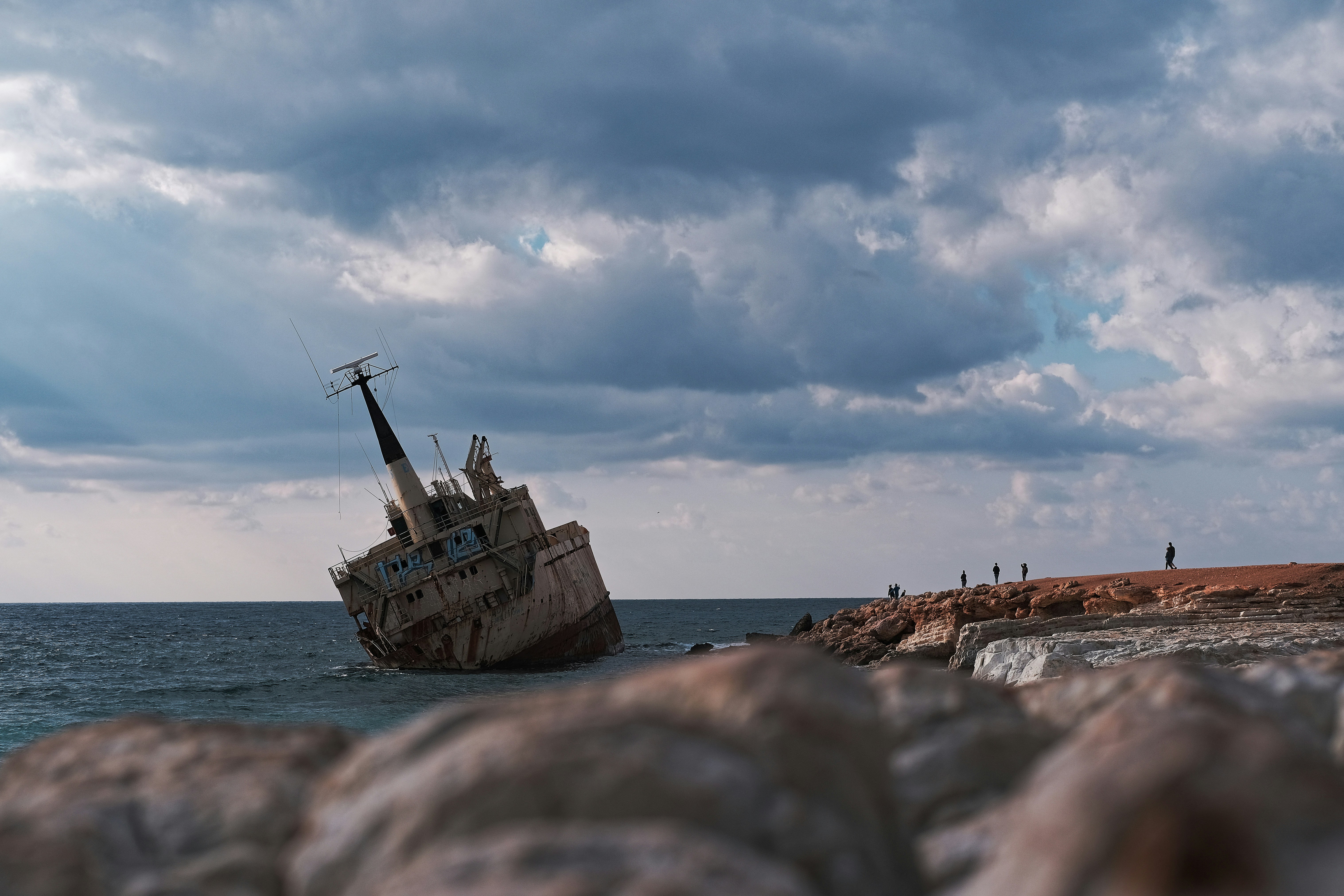 A shipwreck rests on the shore under cloudy skies.