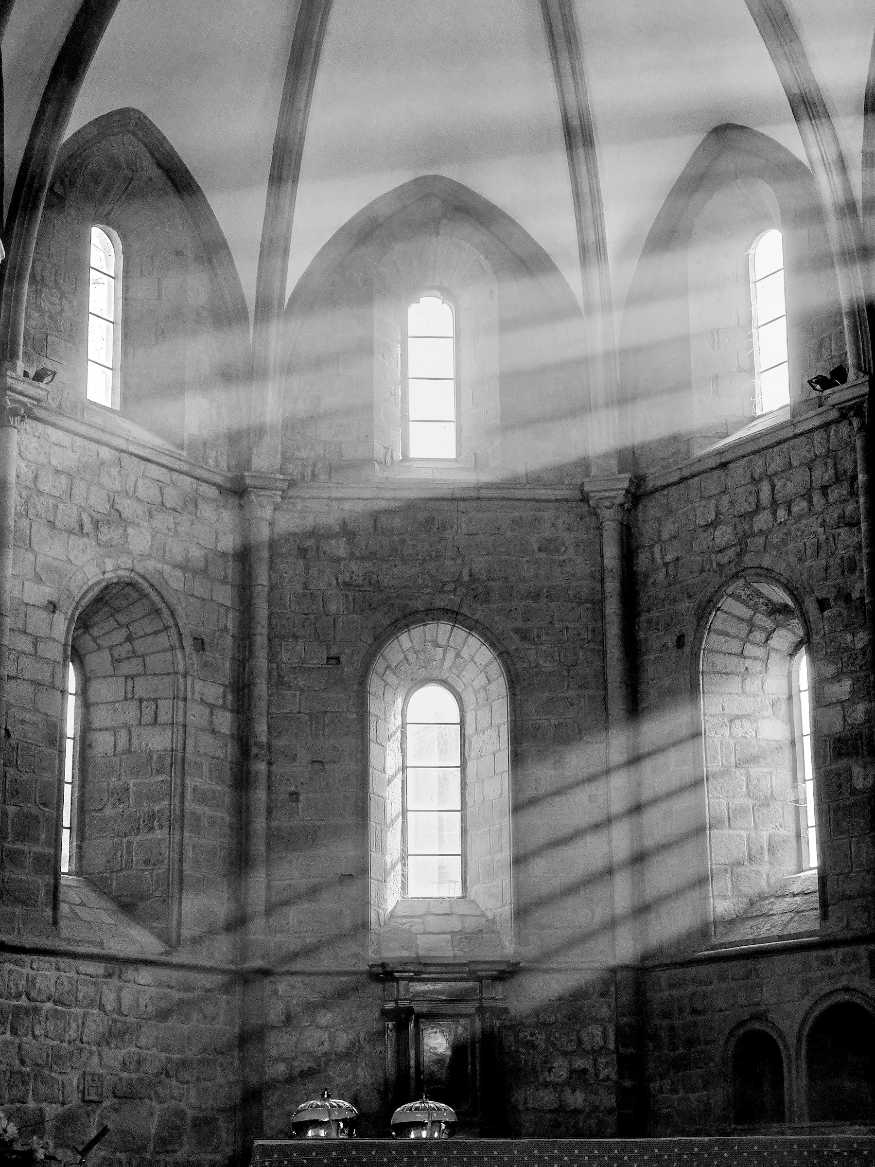 Beams of light falling through arched windows onto a stone wall