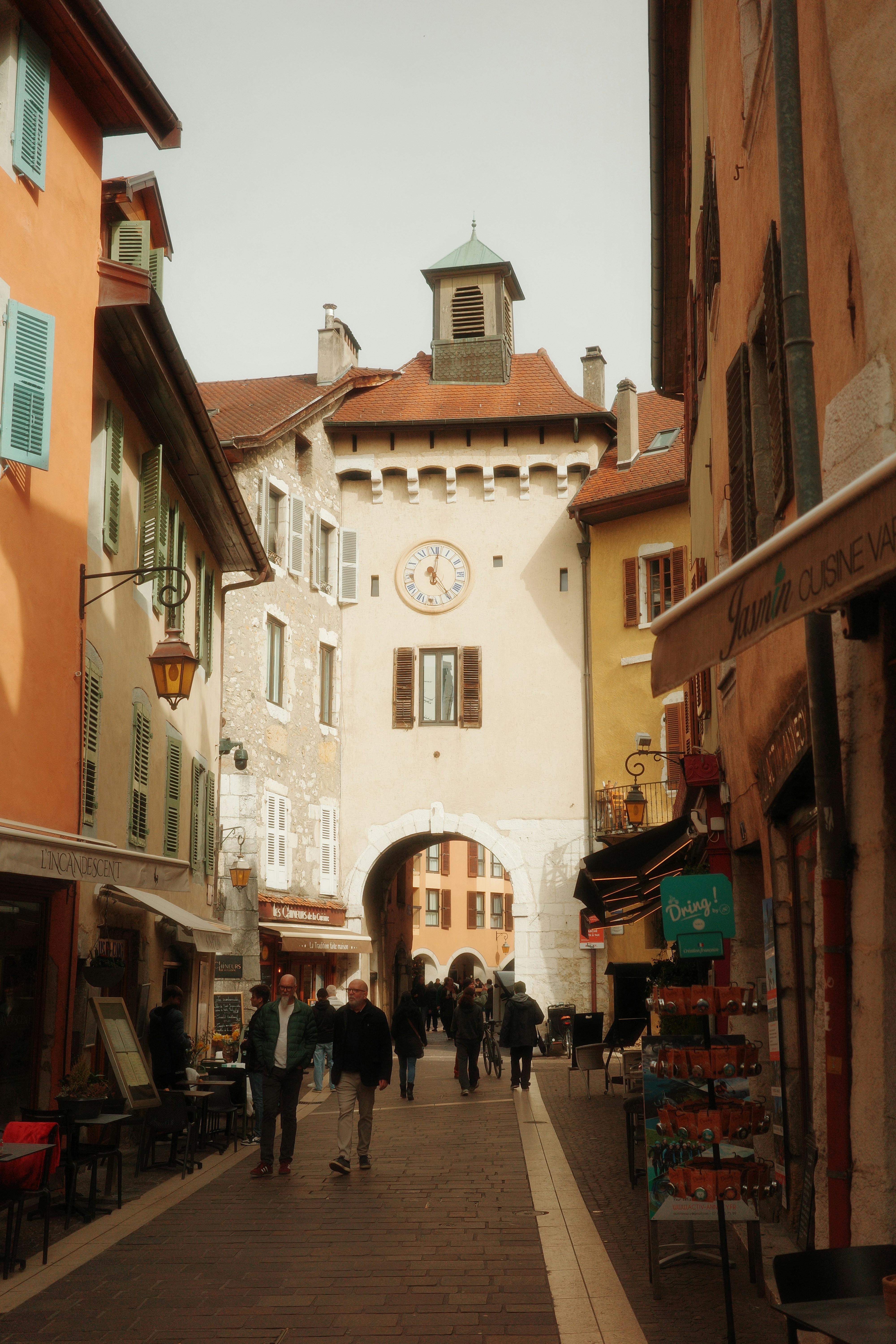 People walk down a narrow street towards a clock tower.