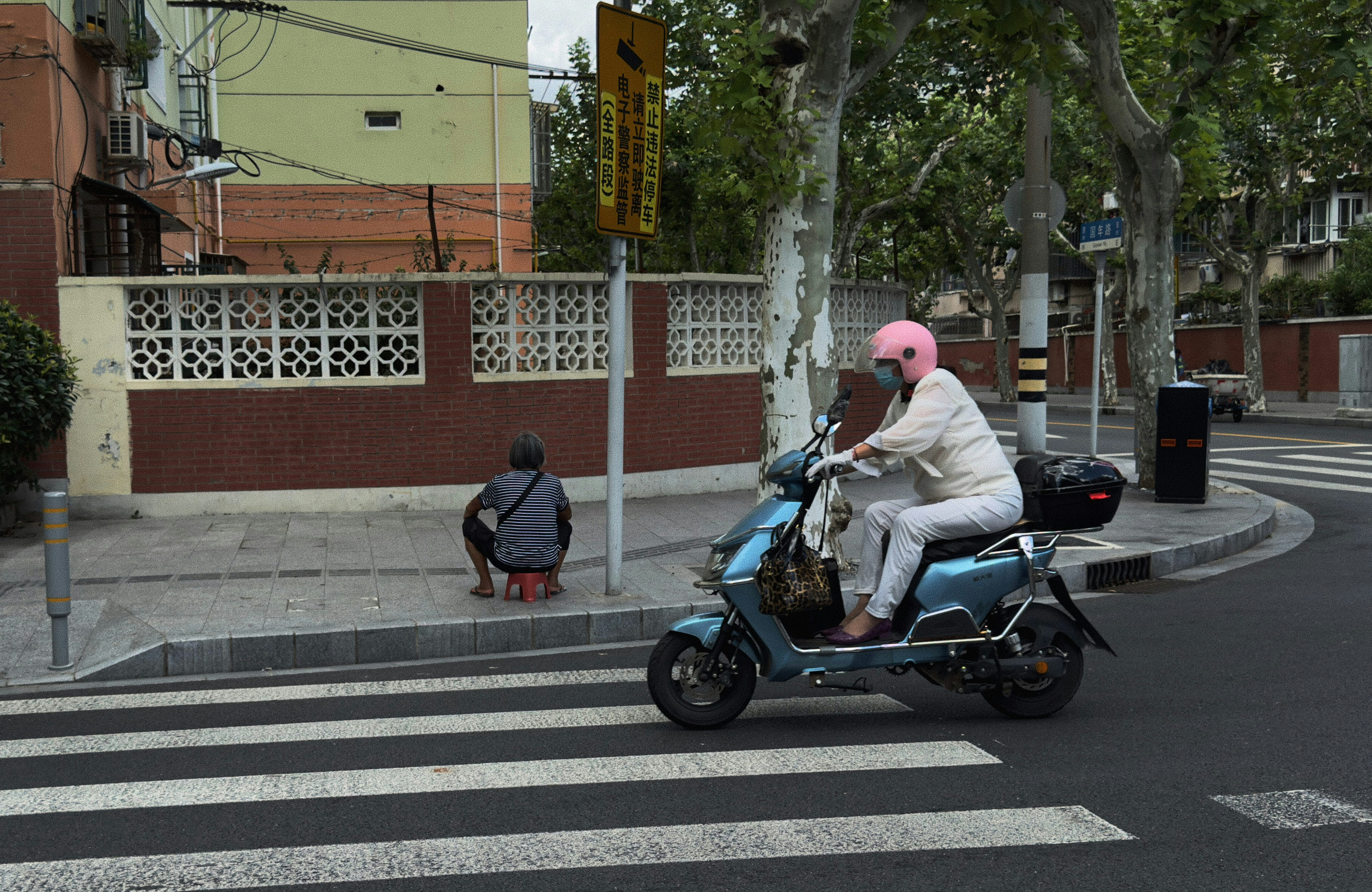 Woman rides scooter past pedestrian crossing on street.