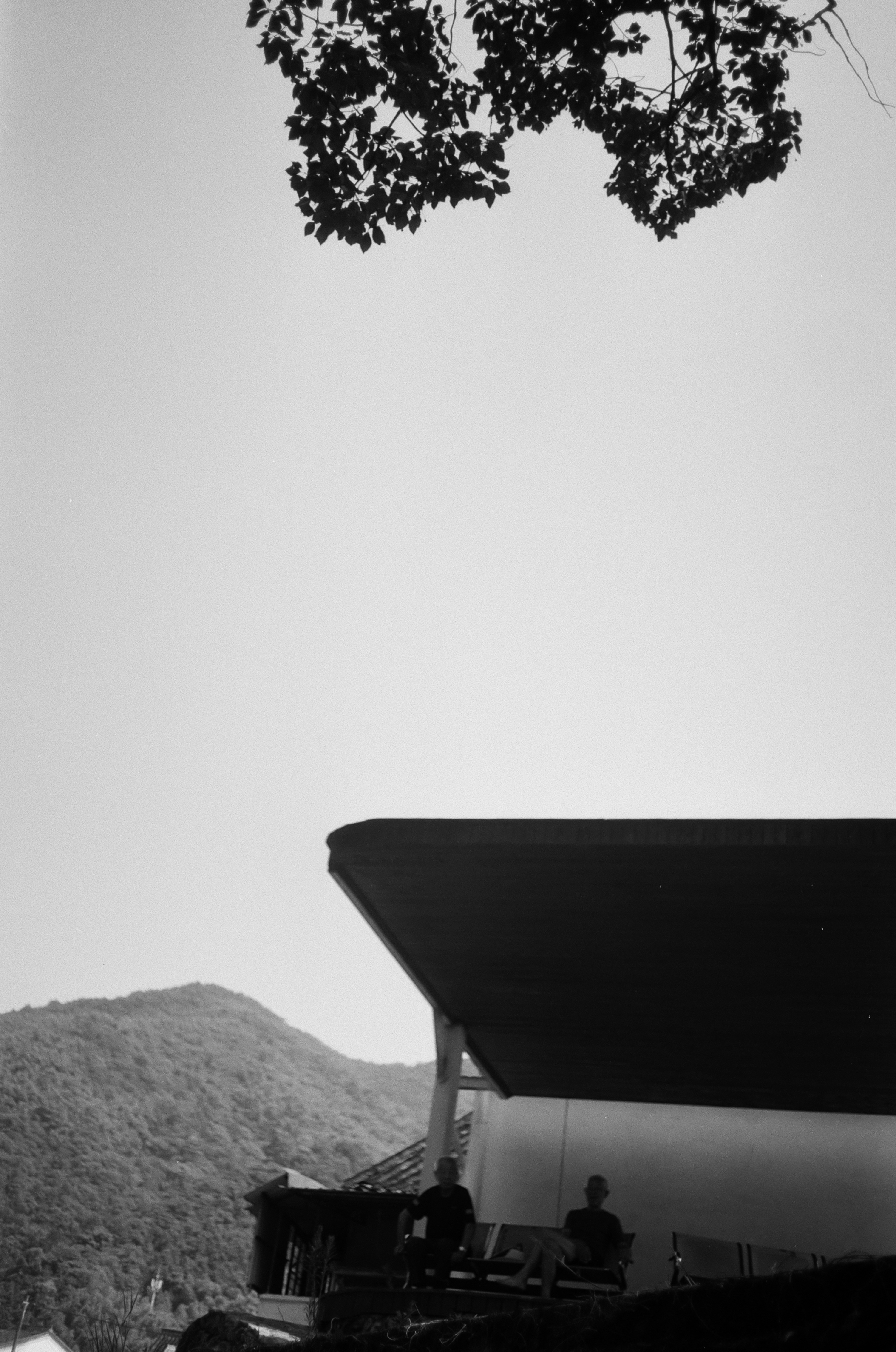 Two people sit on a porch with mountains behind.
