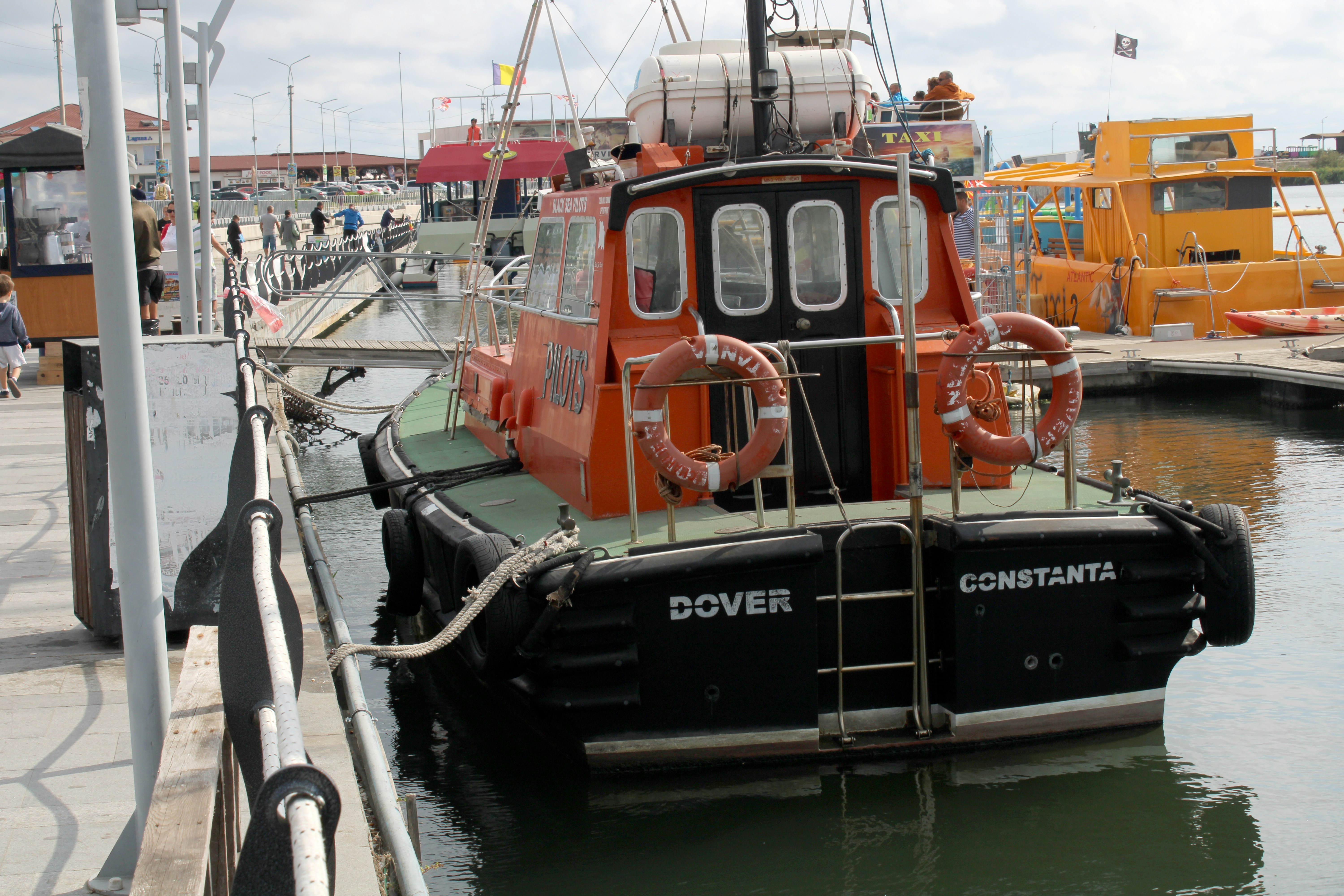 Rebocador laranja atracado em um píer com outros barcos.