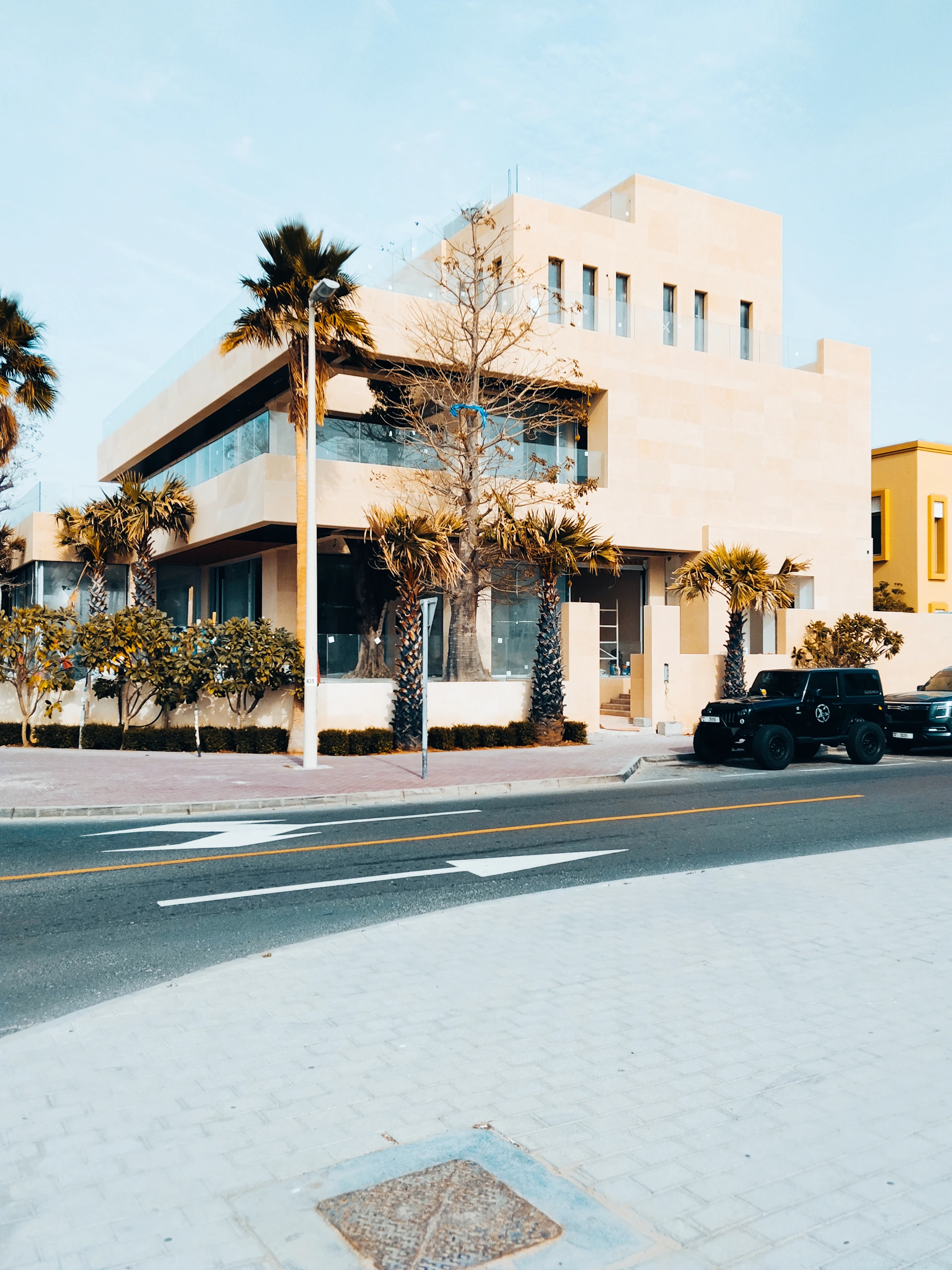 Modern beige building with palm trees and parked cars.