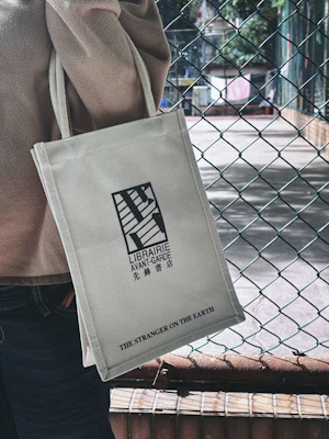 Person holding a canvas tote bag with text and logo.