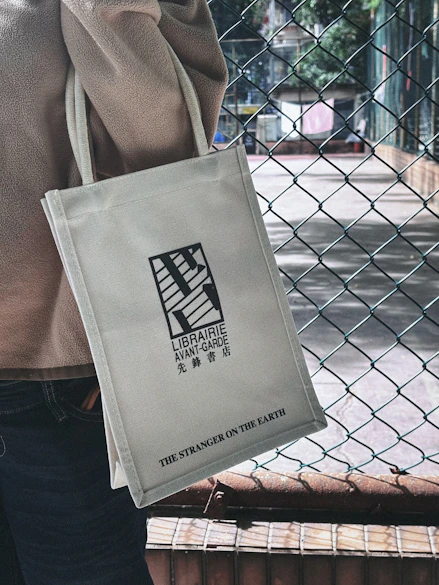 Person holding a canvas tote bag with text and logo.