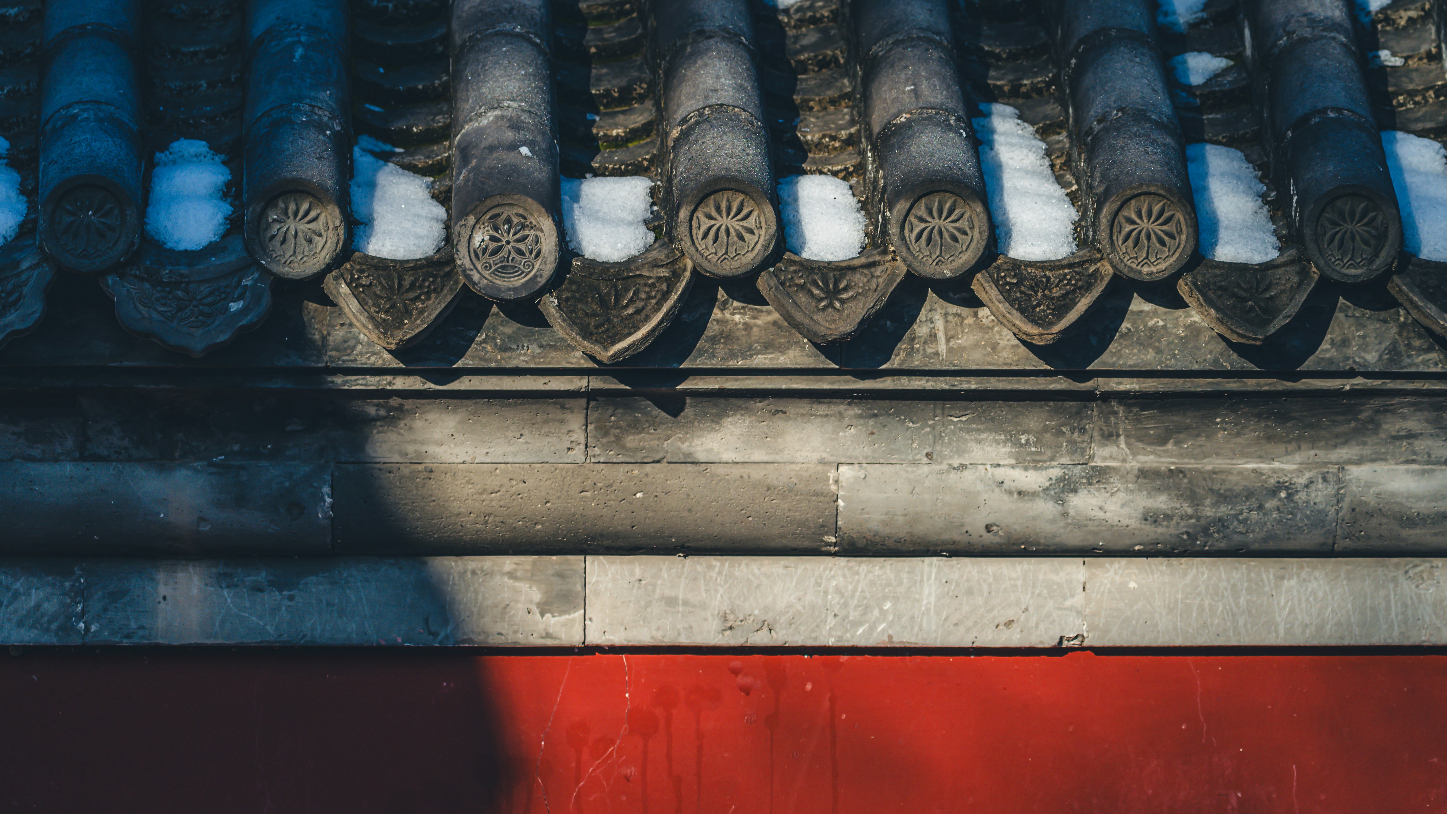 Nahaufnahme eines schneebedeckten Ziegeldachs mit roter Wand darunter.