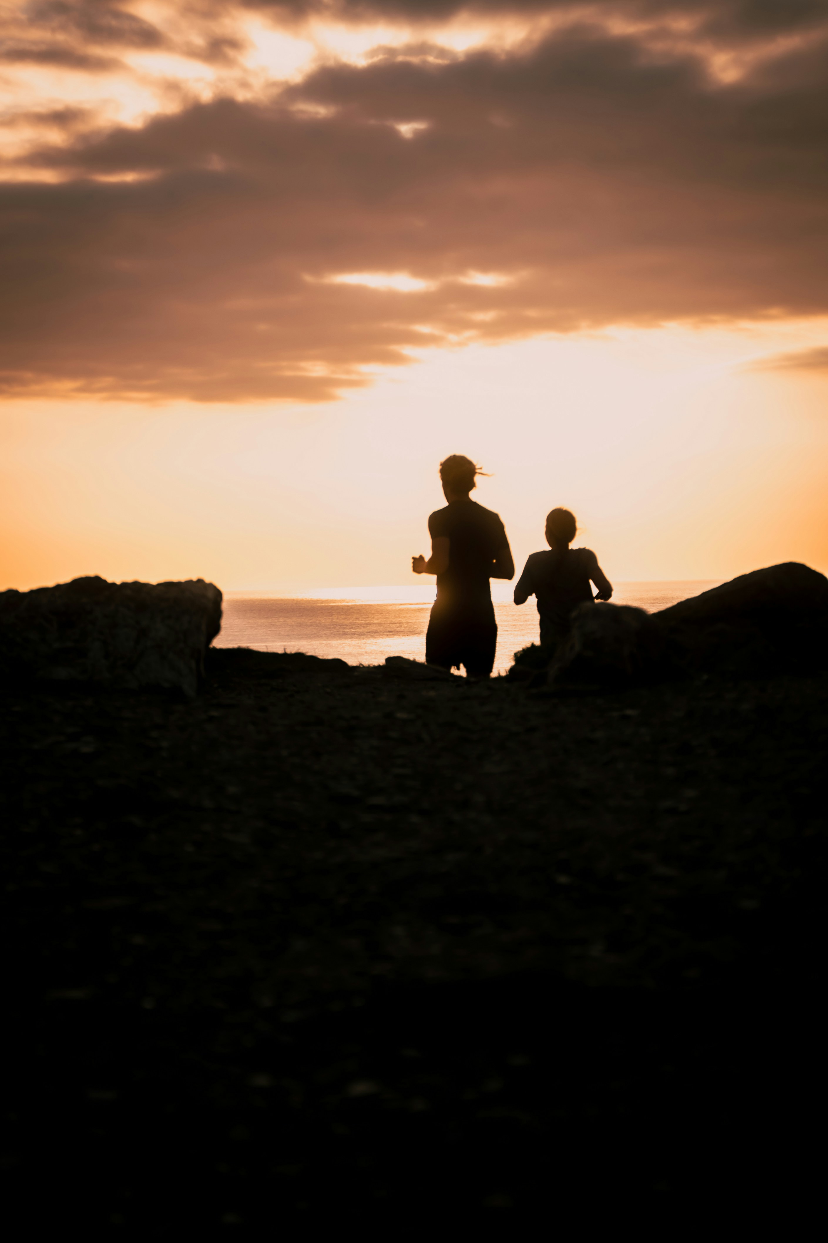 Two people running by the ocean at sunset