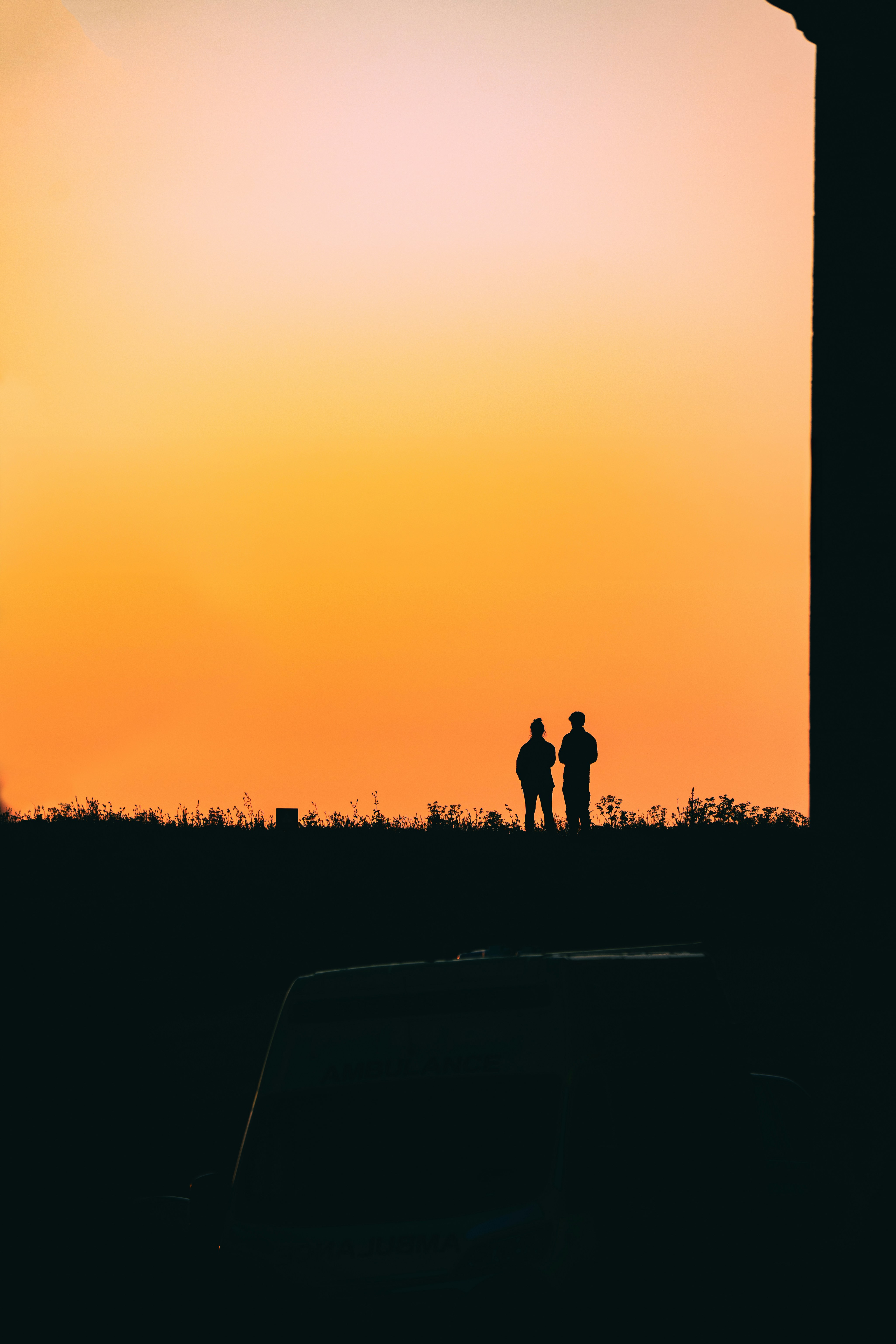 Two people stand silhouetted against an orange sunset sky.