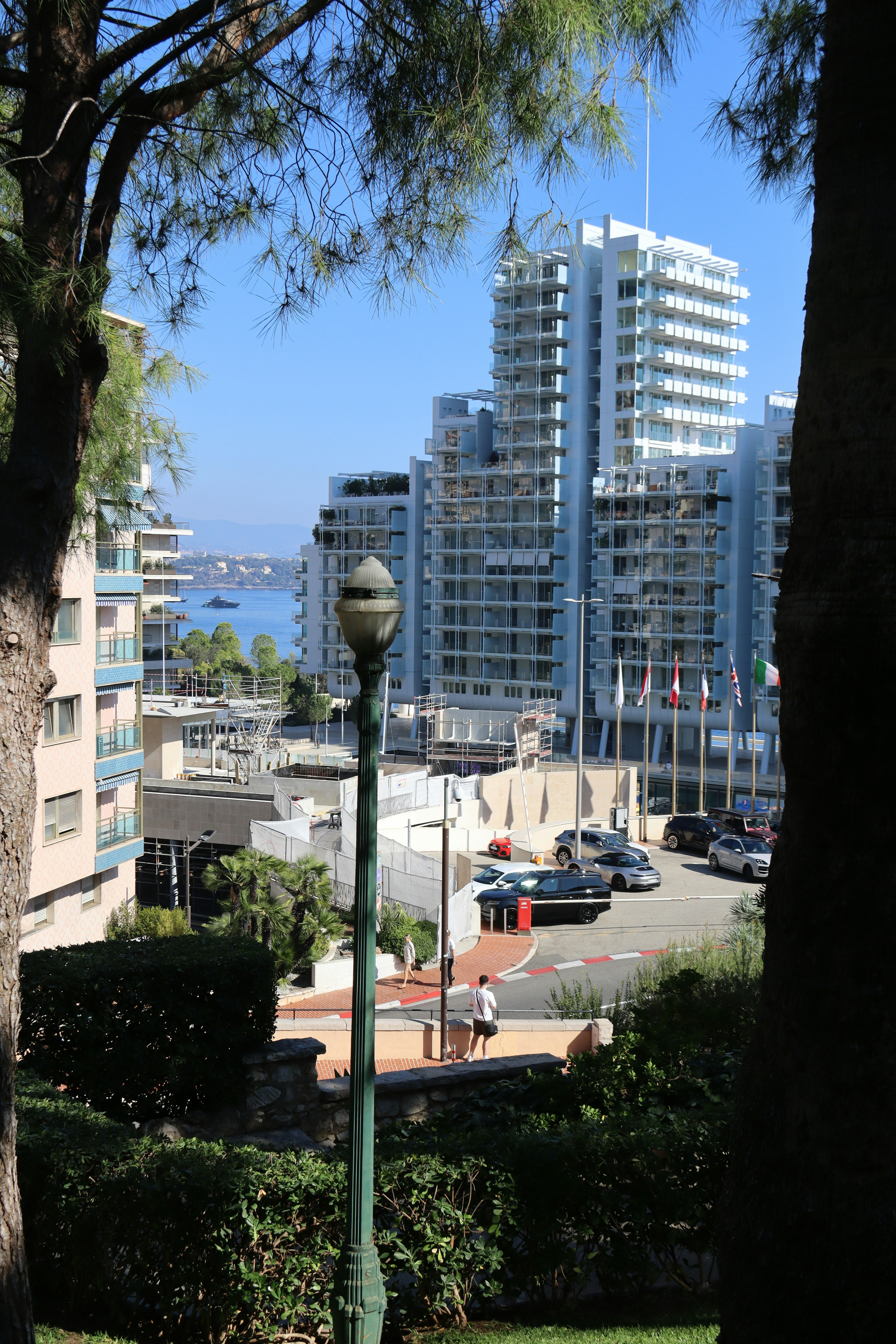 Modern buildings overlook a street with cars and the ocean.