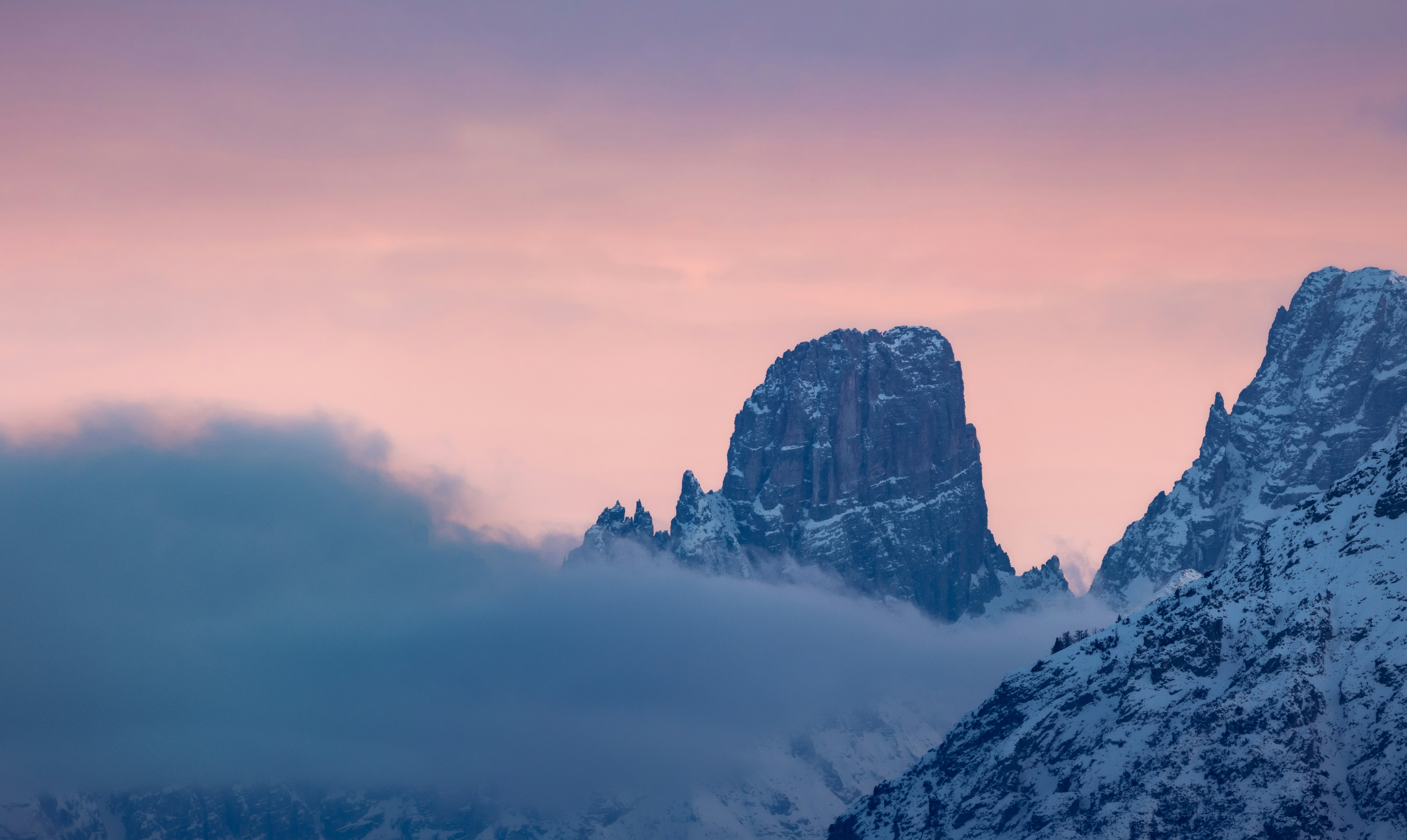 Snowy mountain peaks under a soft pink sky