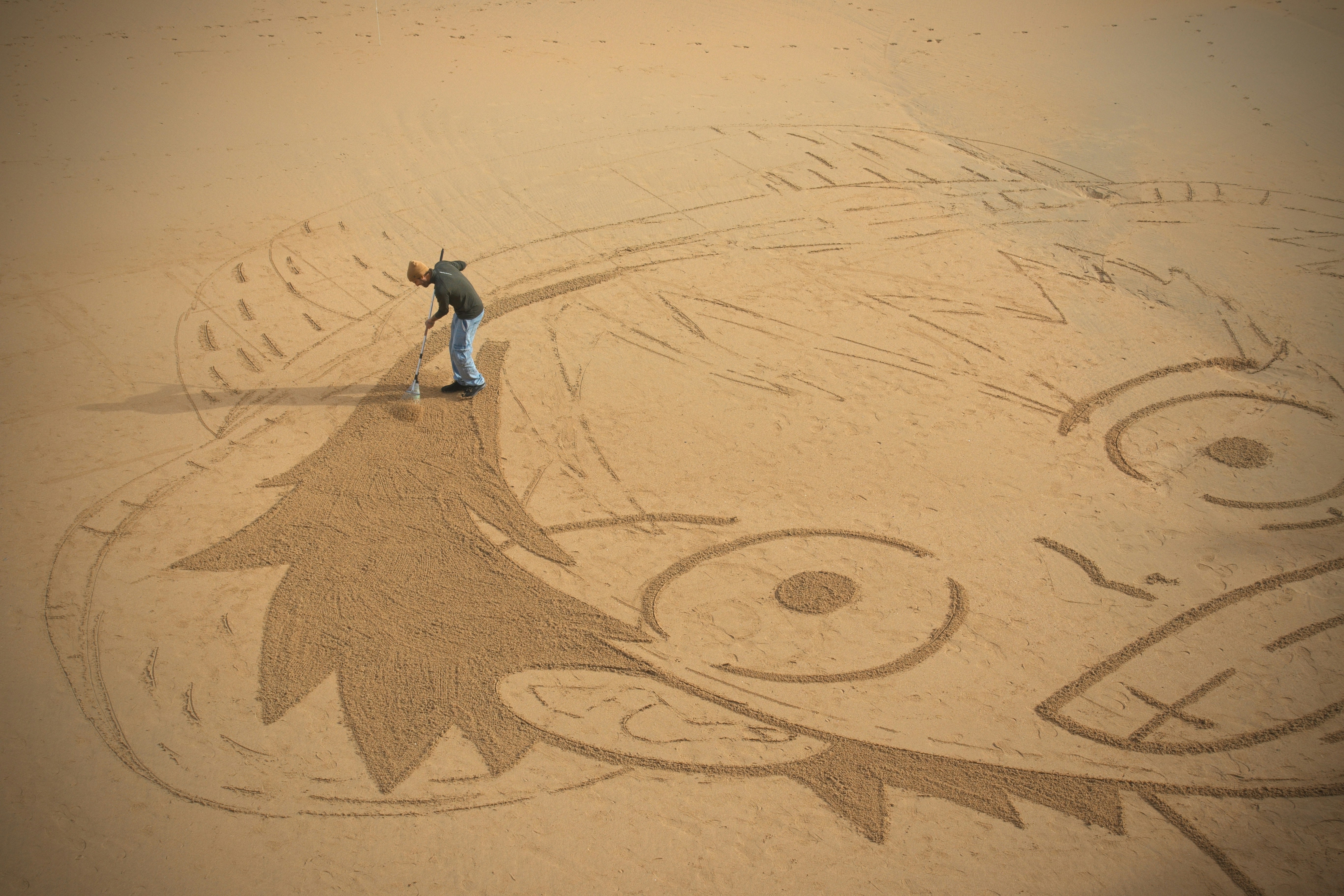 Man drawing large cartoon face in sand