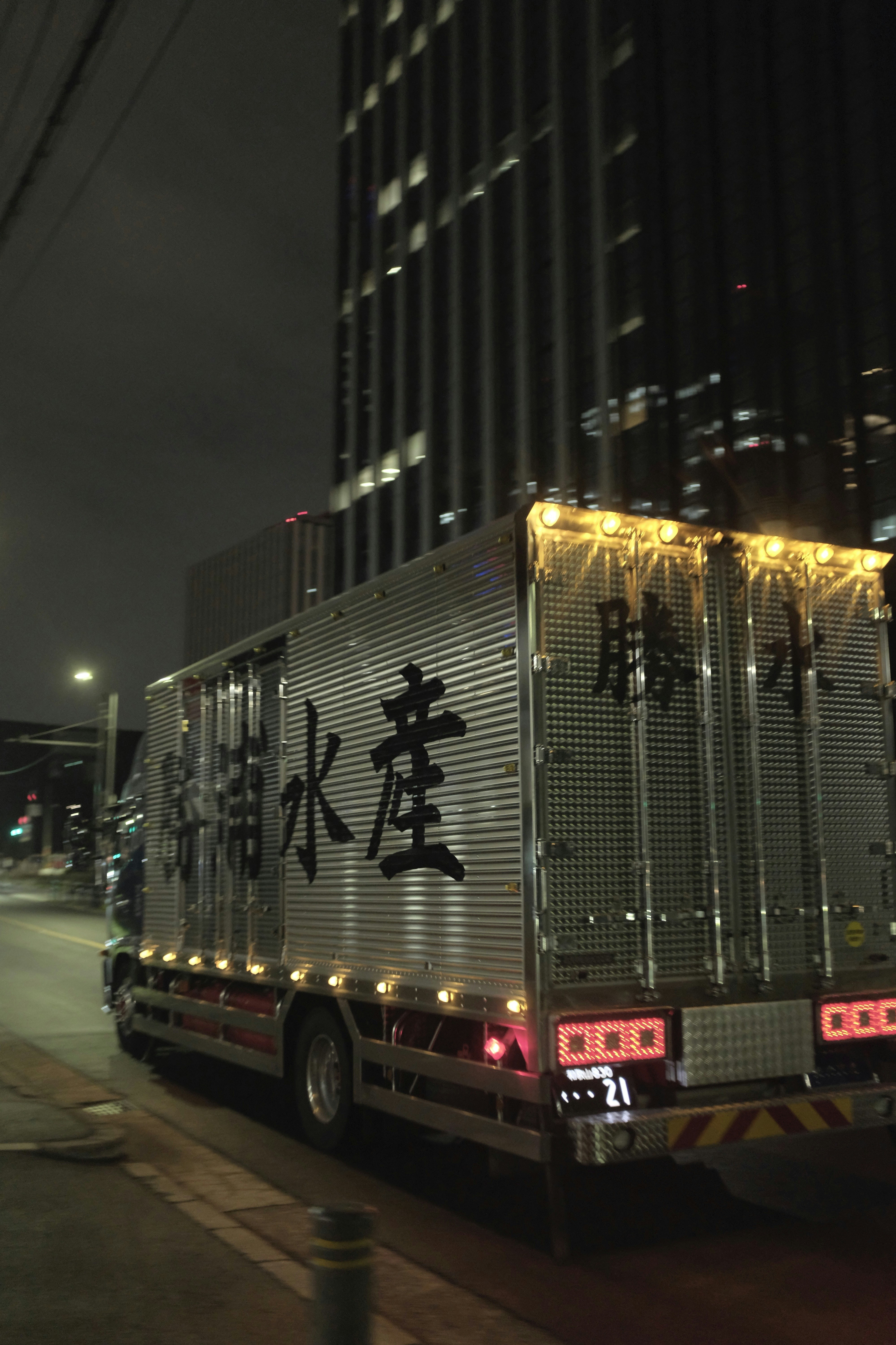 A delivery truck drives down a city street at night.