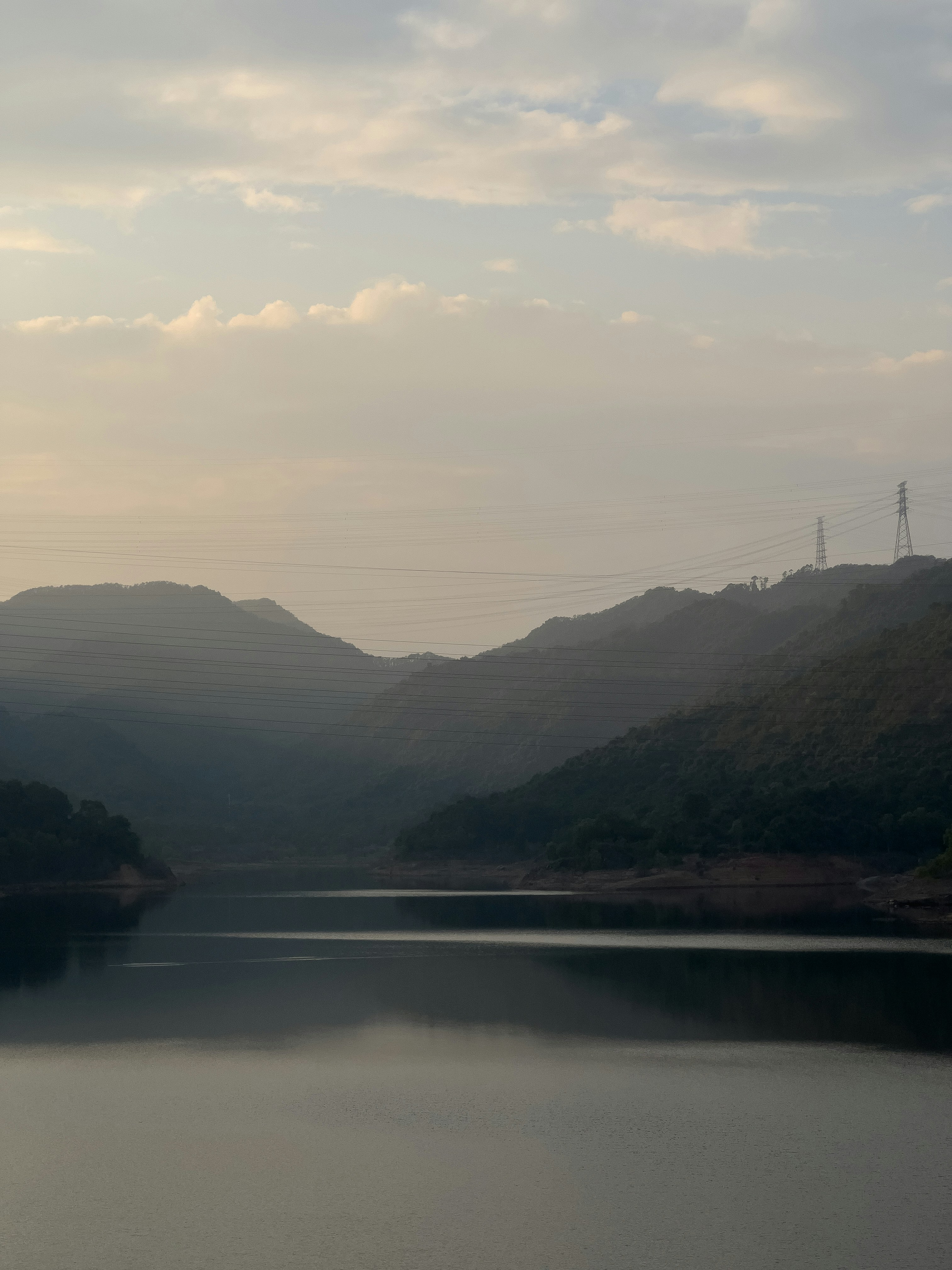Neblige Berge spiegeln sich in einem ruhigen See bei Einbruch der Dämmerung.