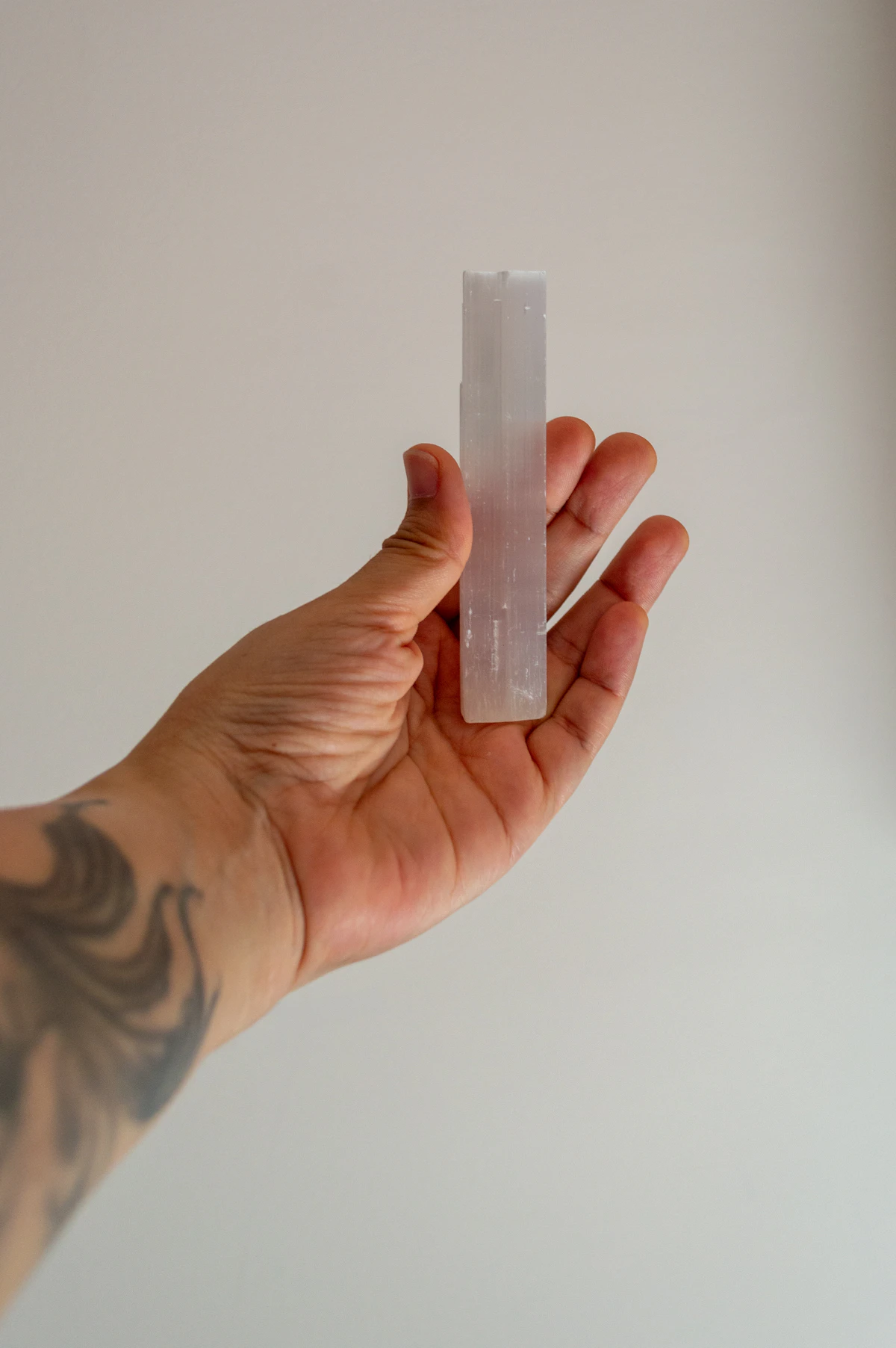 A hand holding a translucent crystal wand against a soft background, illustrating the kind of selenite piece kept beside rose quartz between cleansings
