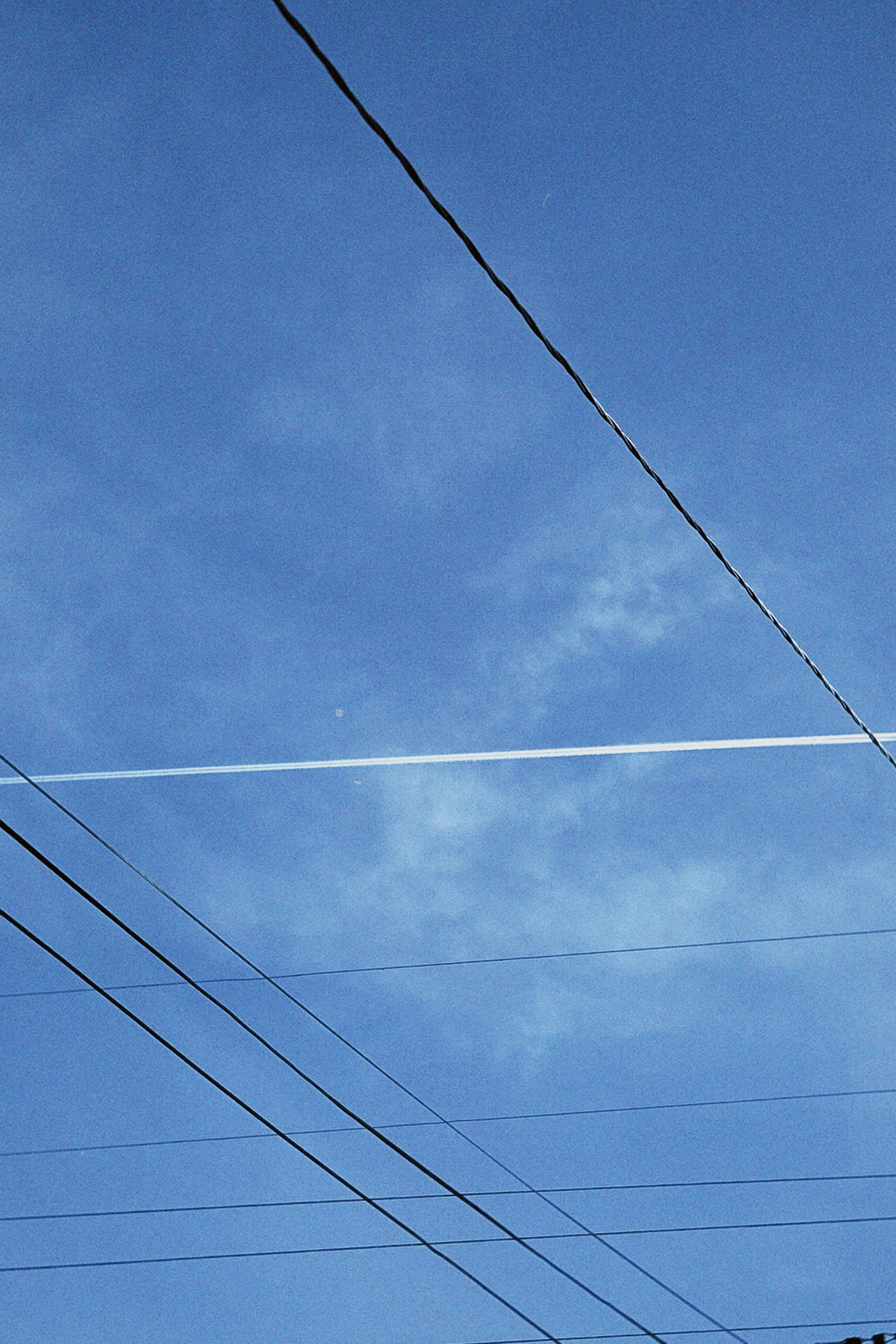 Klarer blauer Himmel mit dünnen Wolken und Stromleitungen