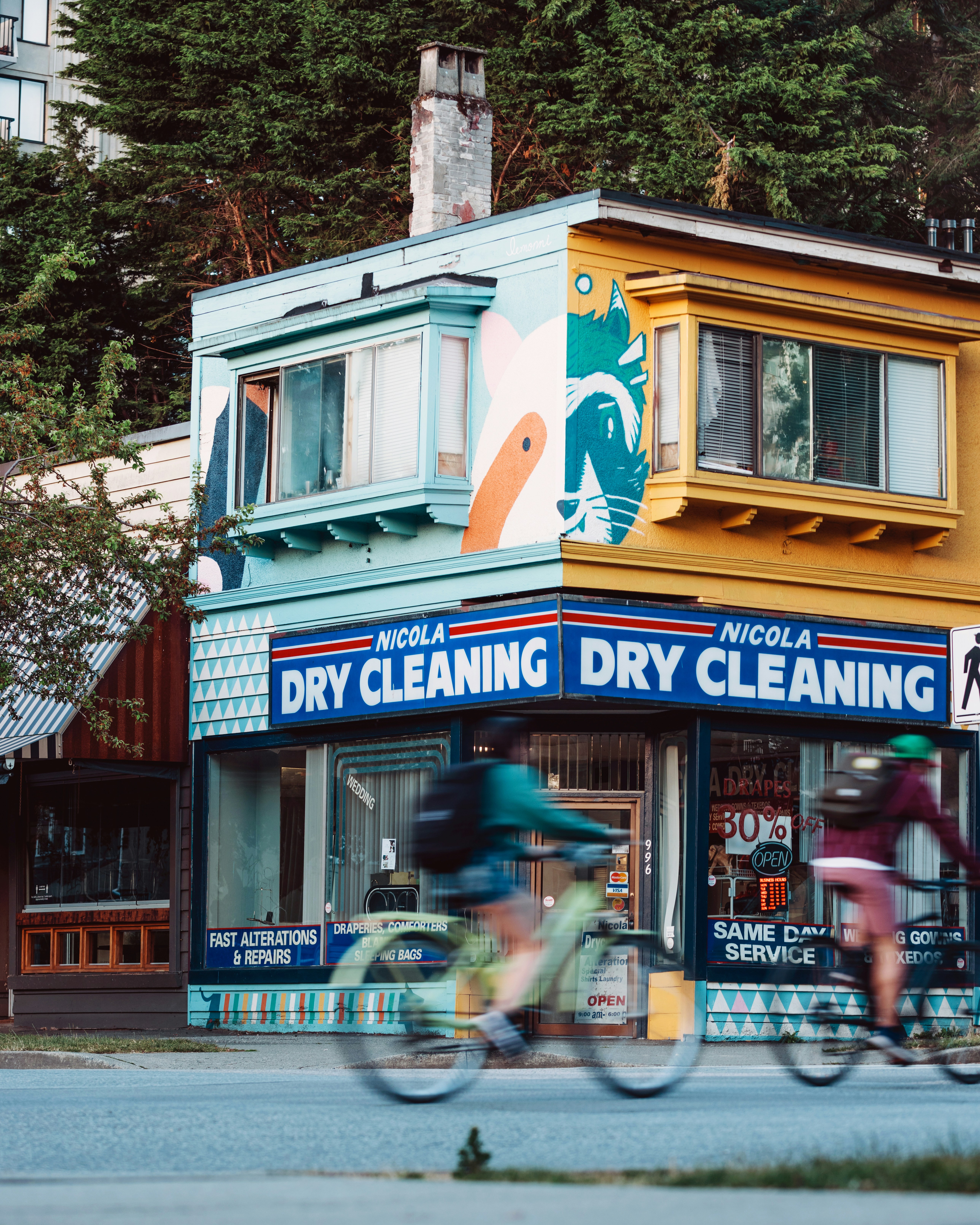 People cycling past a colorful dry cleaning store.