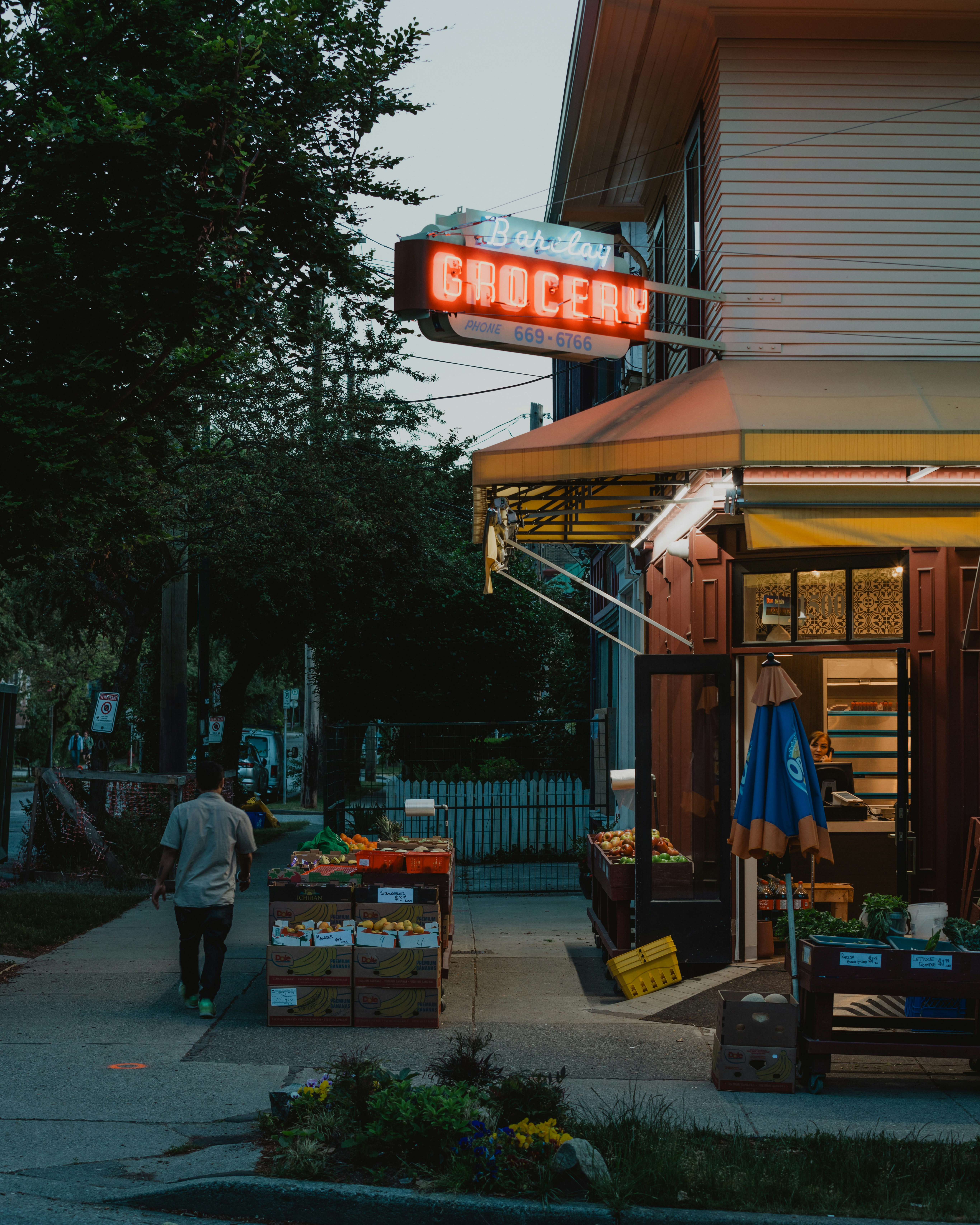 A person walks past a grocery store at dusk.