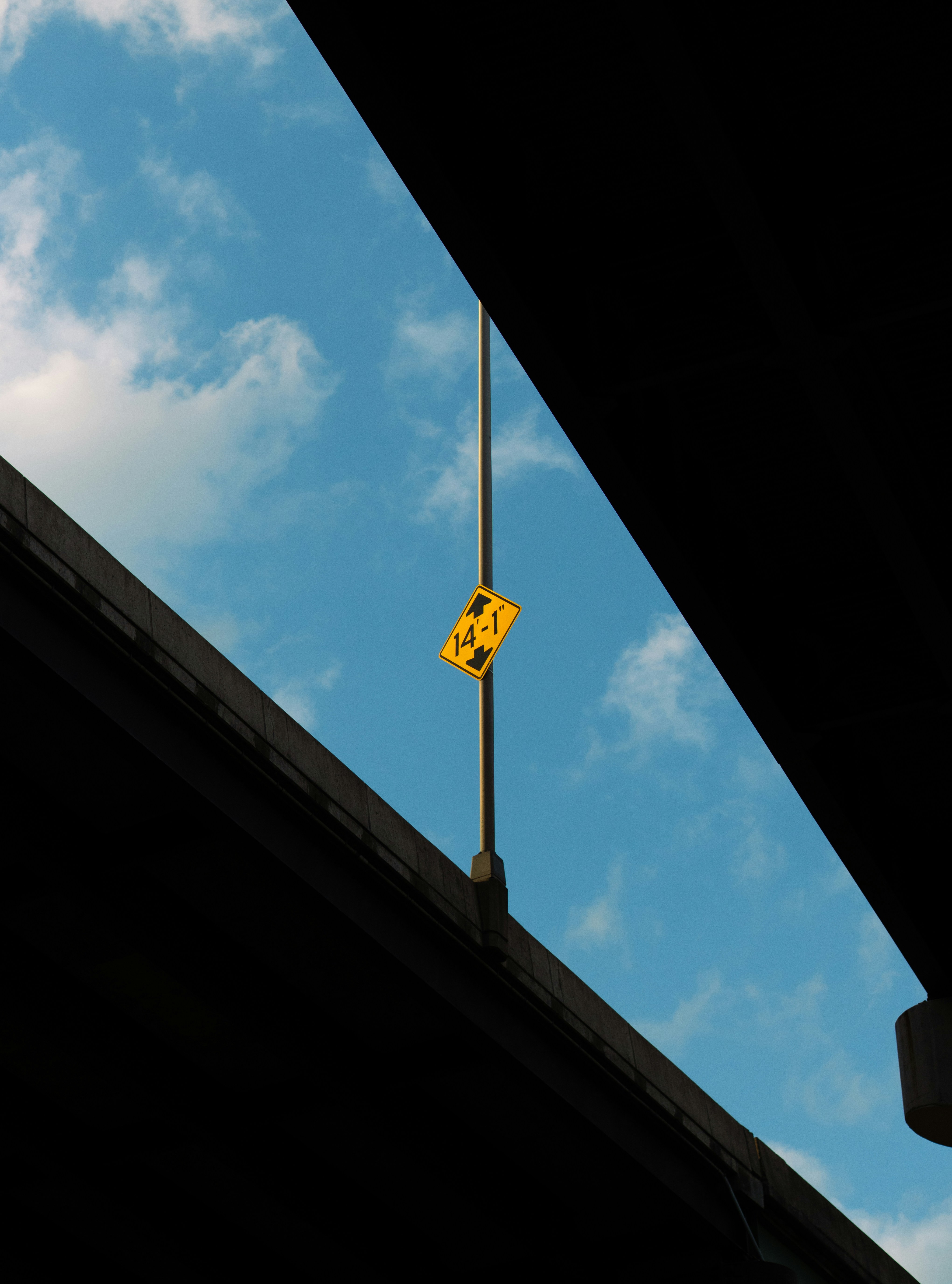 Yellow warning sign hanging from pole against blue sky