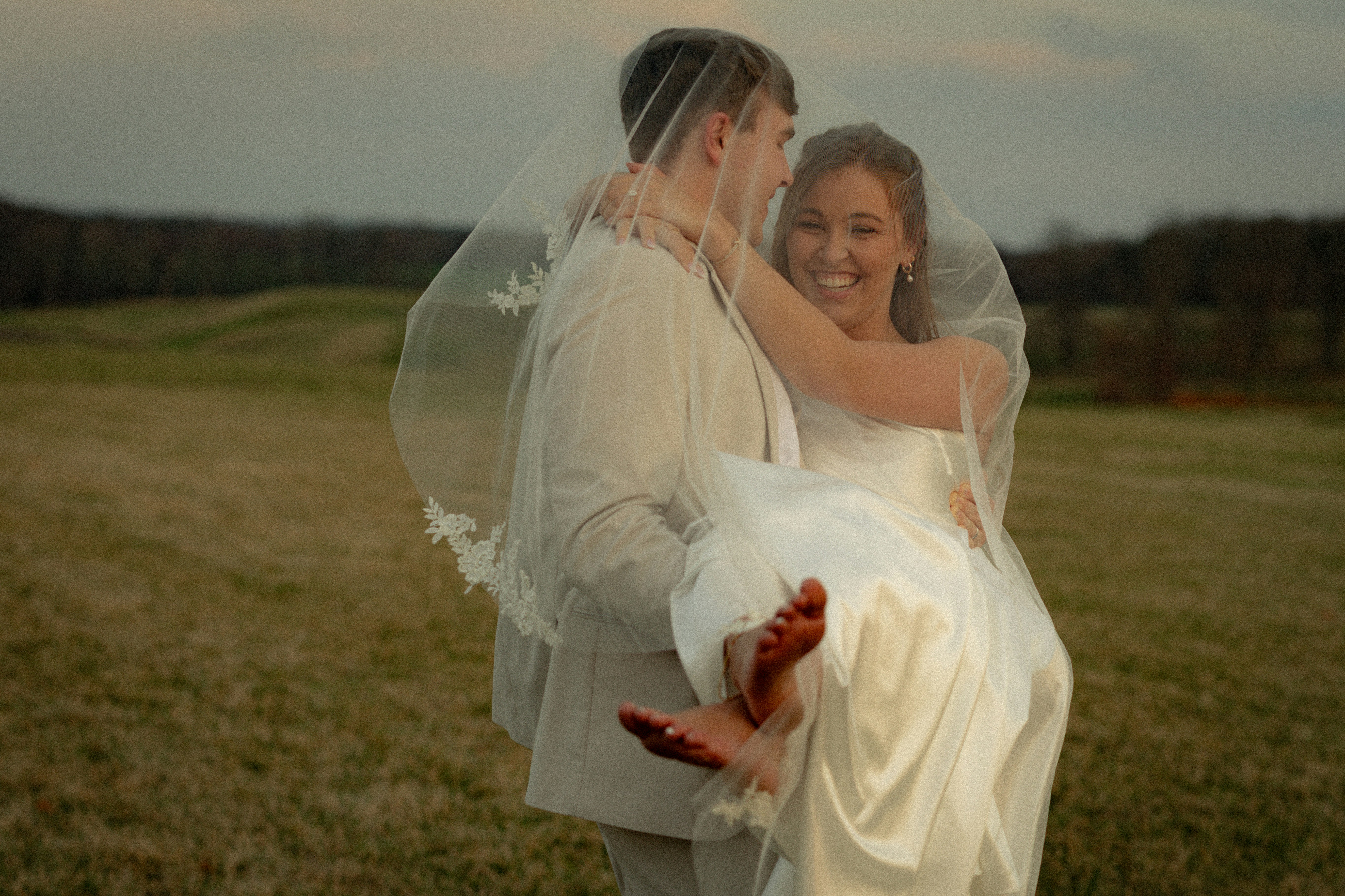 Noivo carrega noiva sob véu em campo gramado