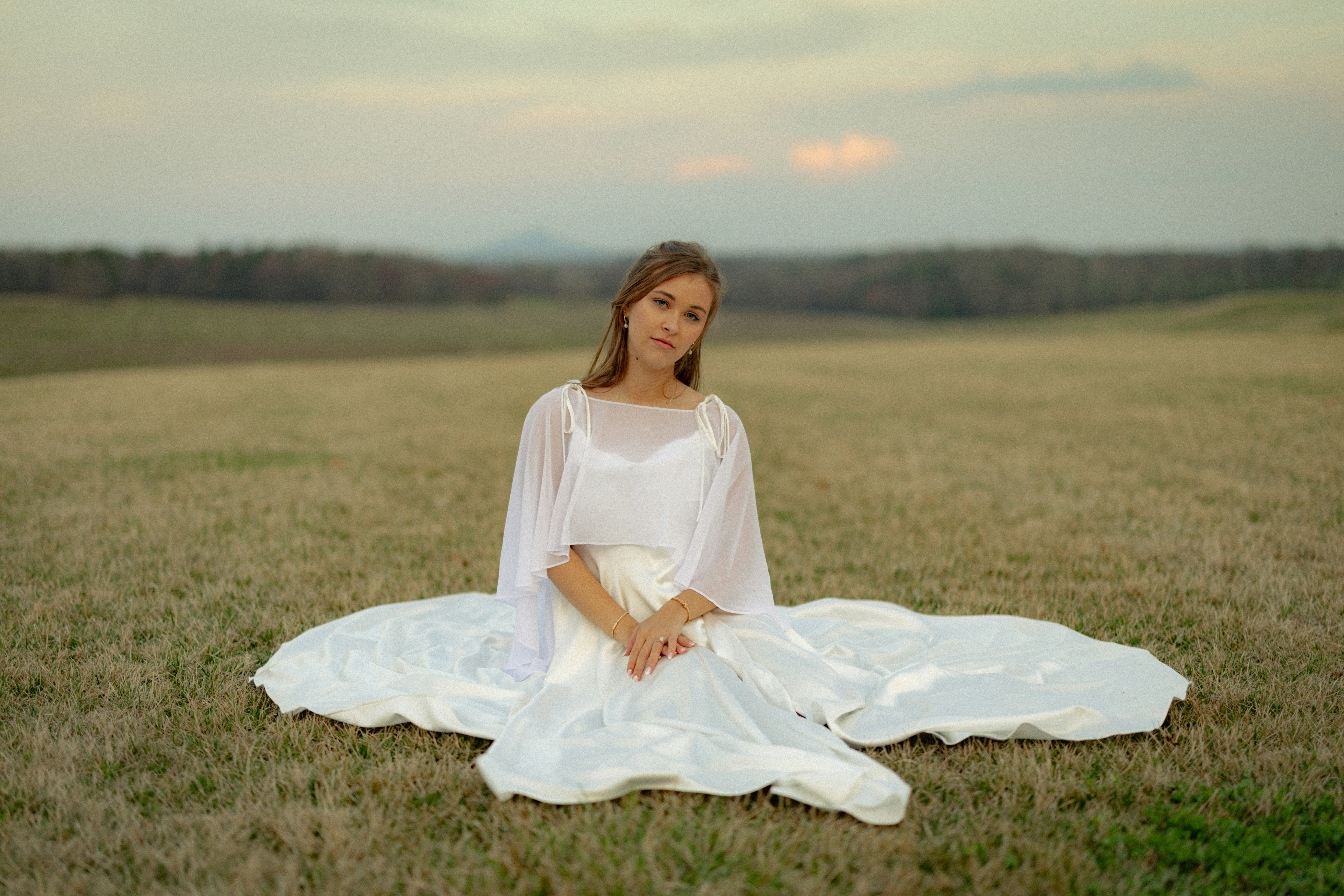 Jovem mulher de vestido branco sentada em um campo.