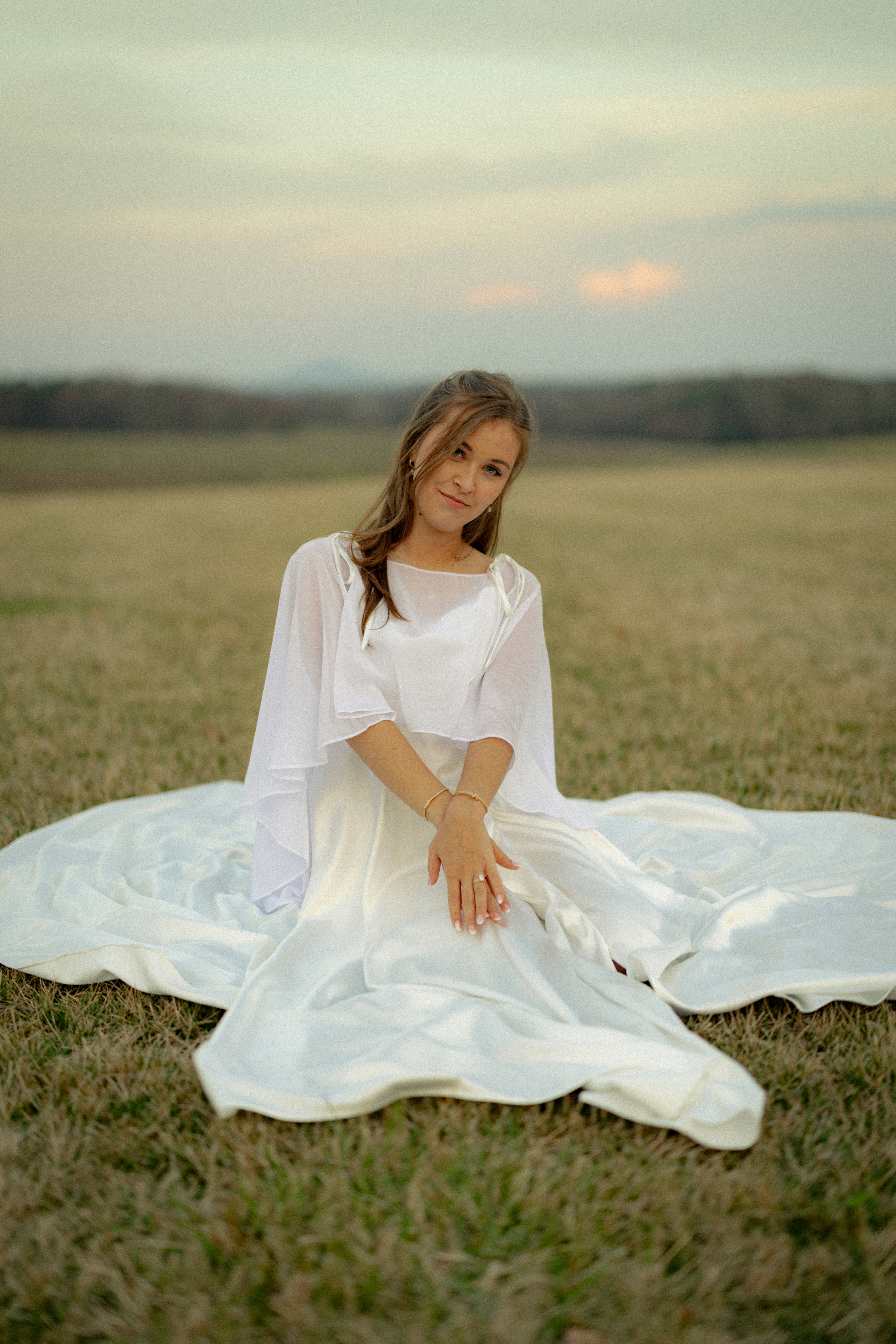 Noiva de vestido branco sentada em um campo ao pôr do sol
