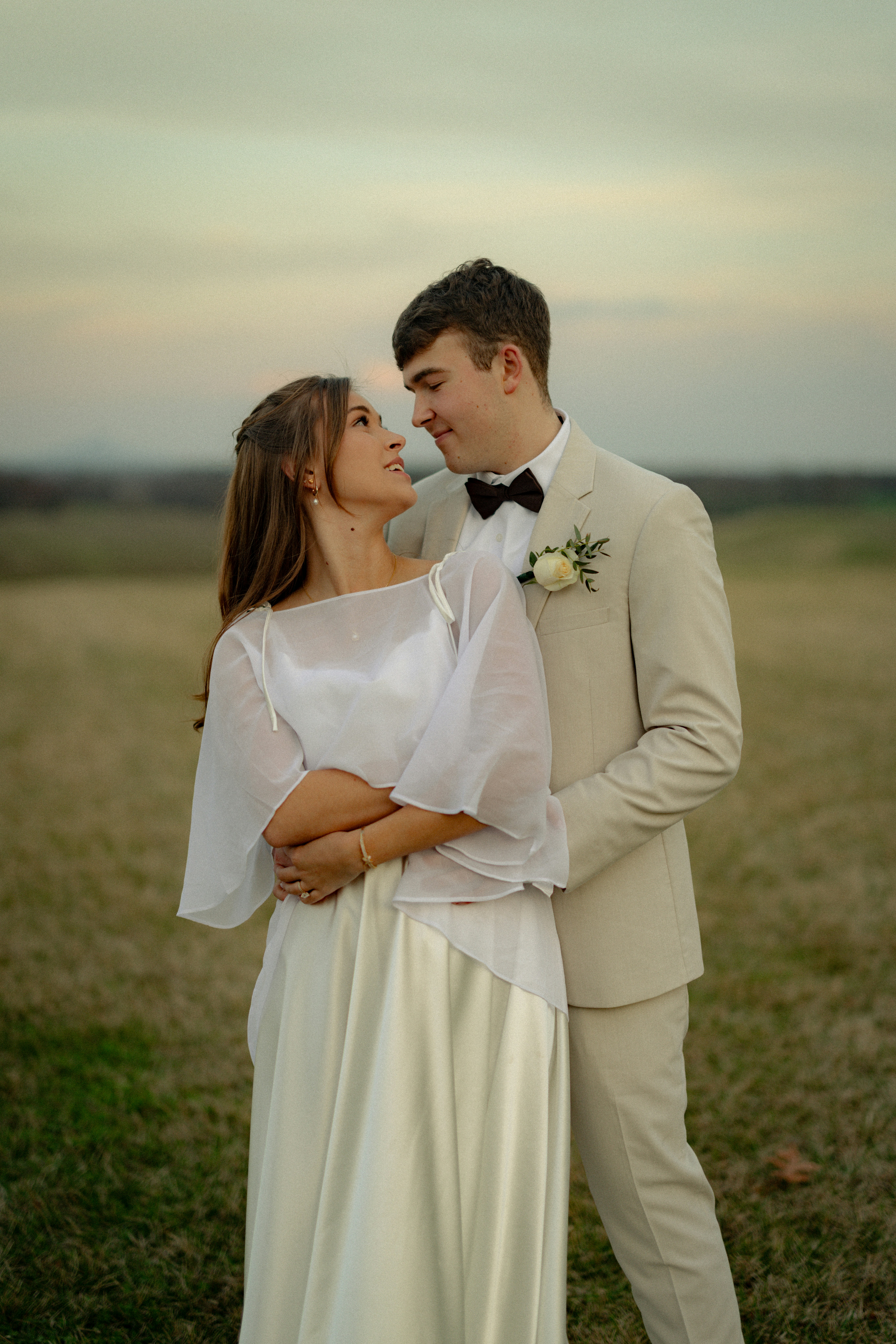 Uma noiva e um noivo se abraçam ao ar livre ao pôr do sol.