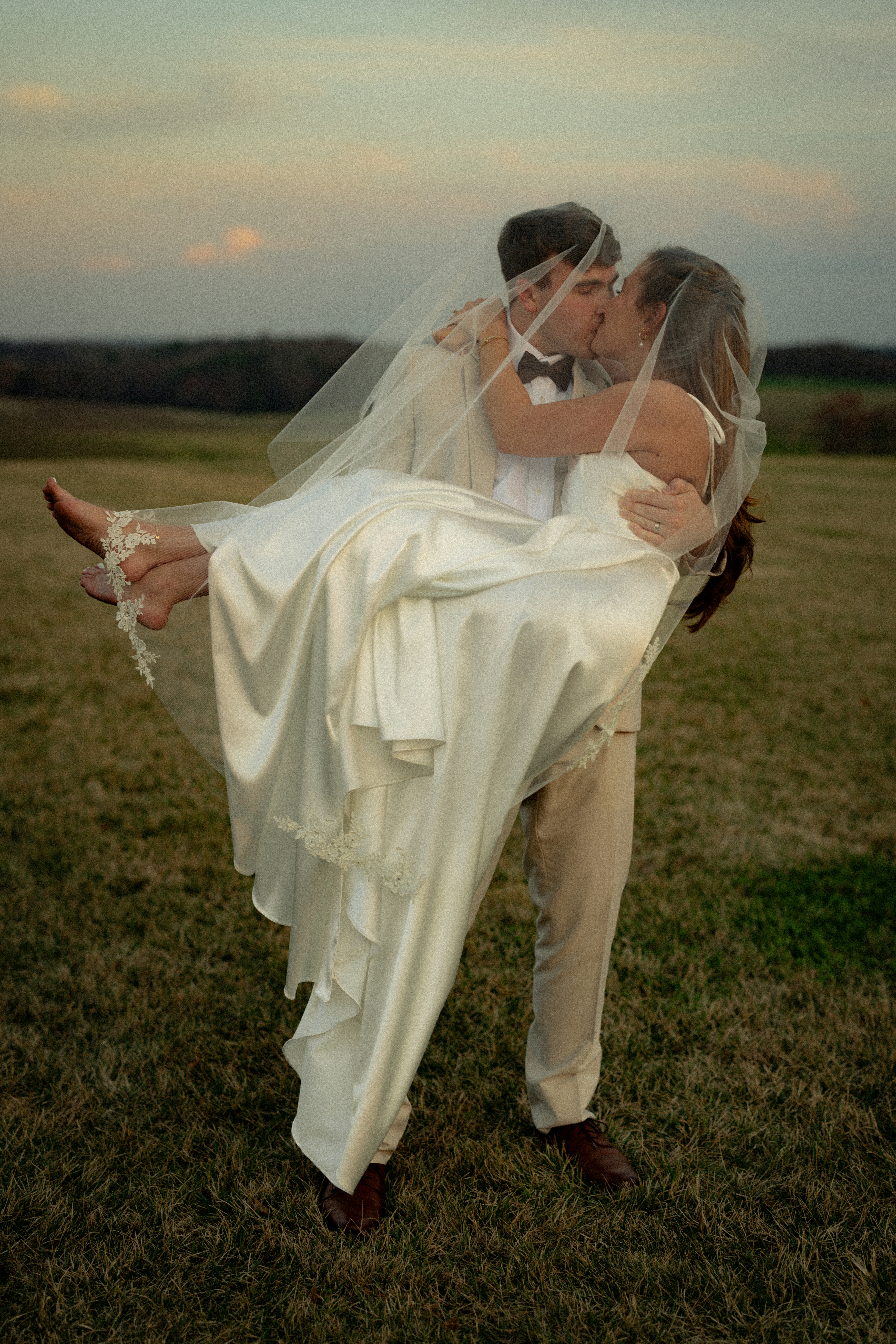 Noivo carregando noiva em um campo ao pôr do sol.
