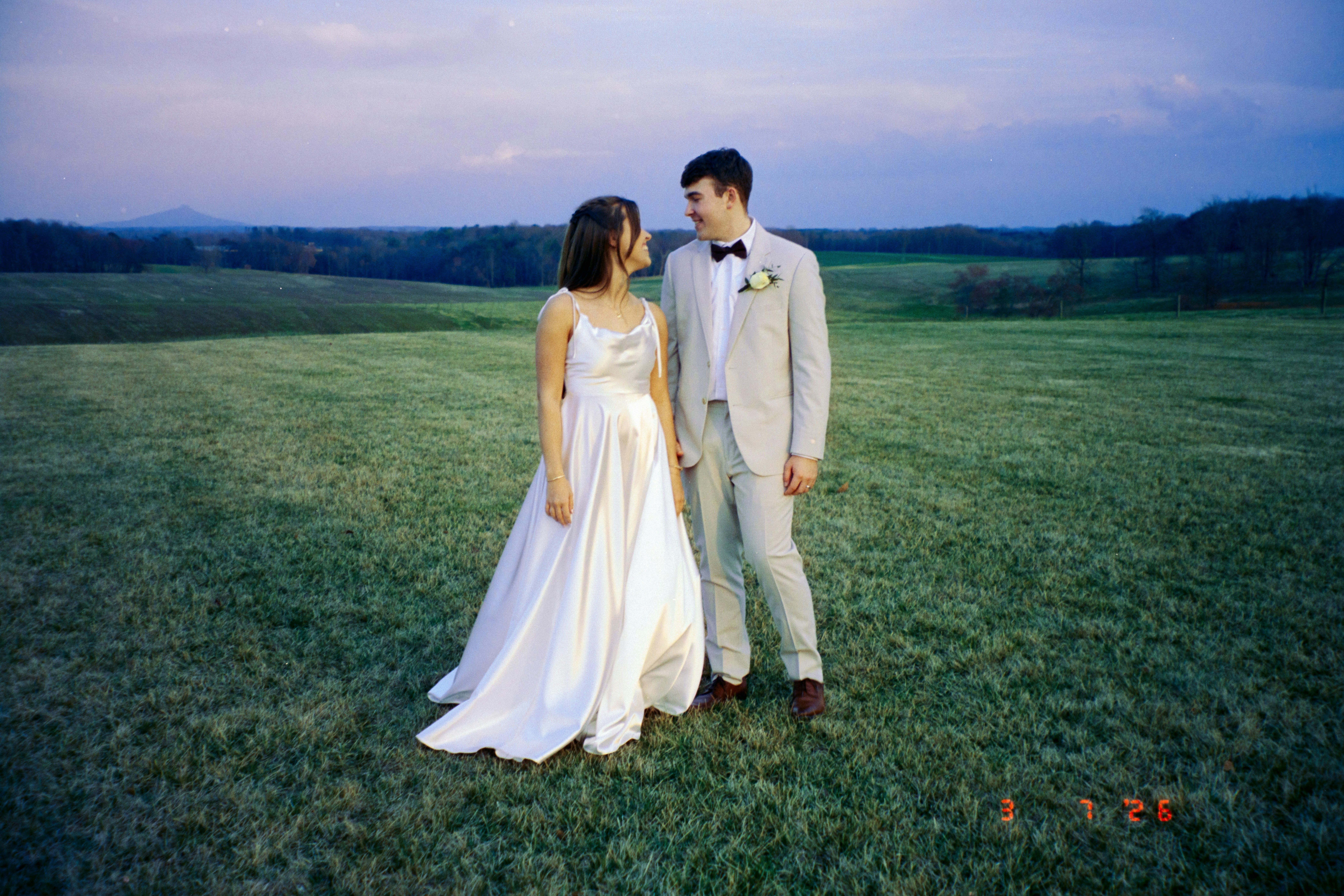 Um casal em traje de casamento parado em um campo gramado.
