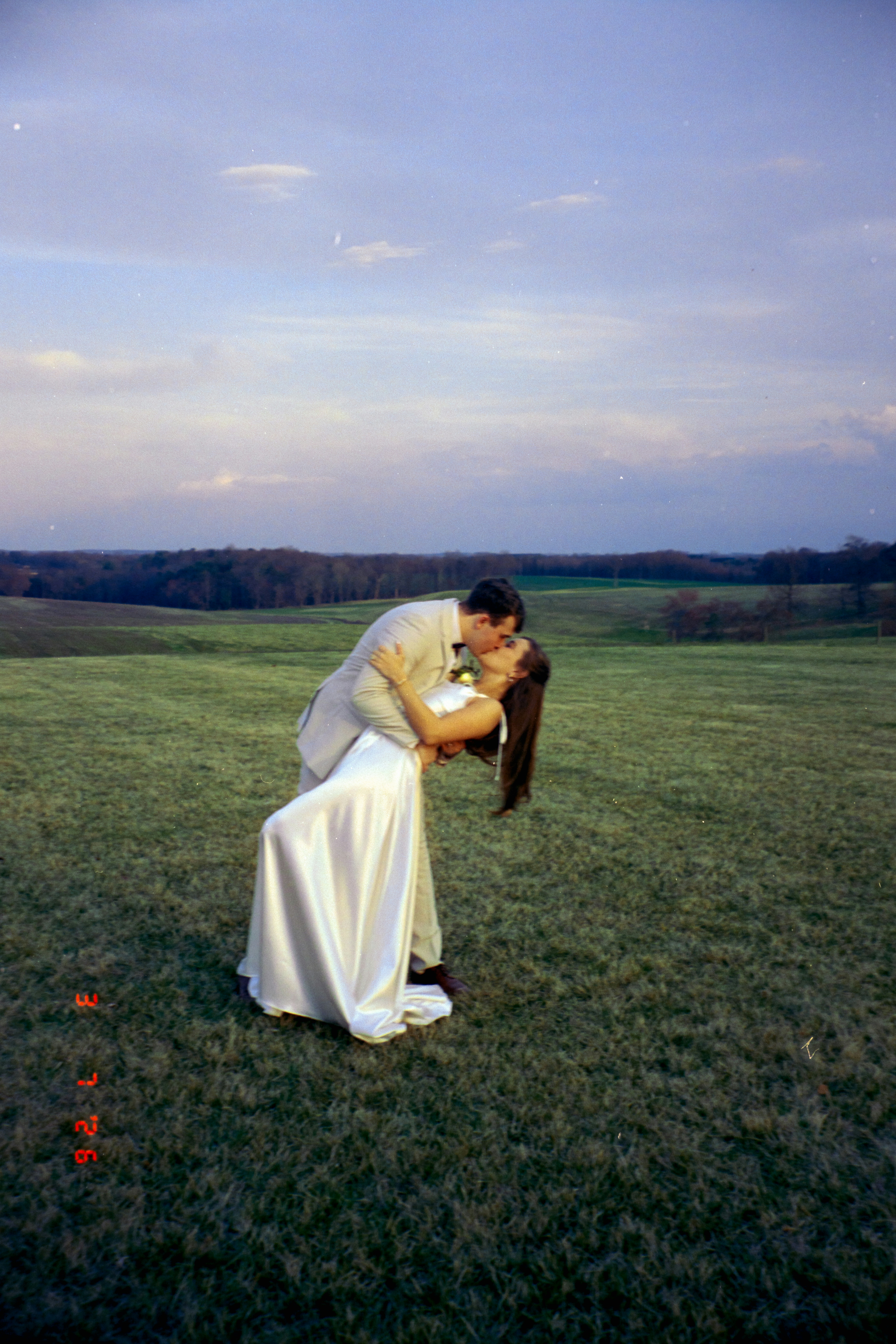 Um casal se beijando em um campo gramado ao pôr do sol