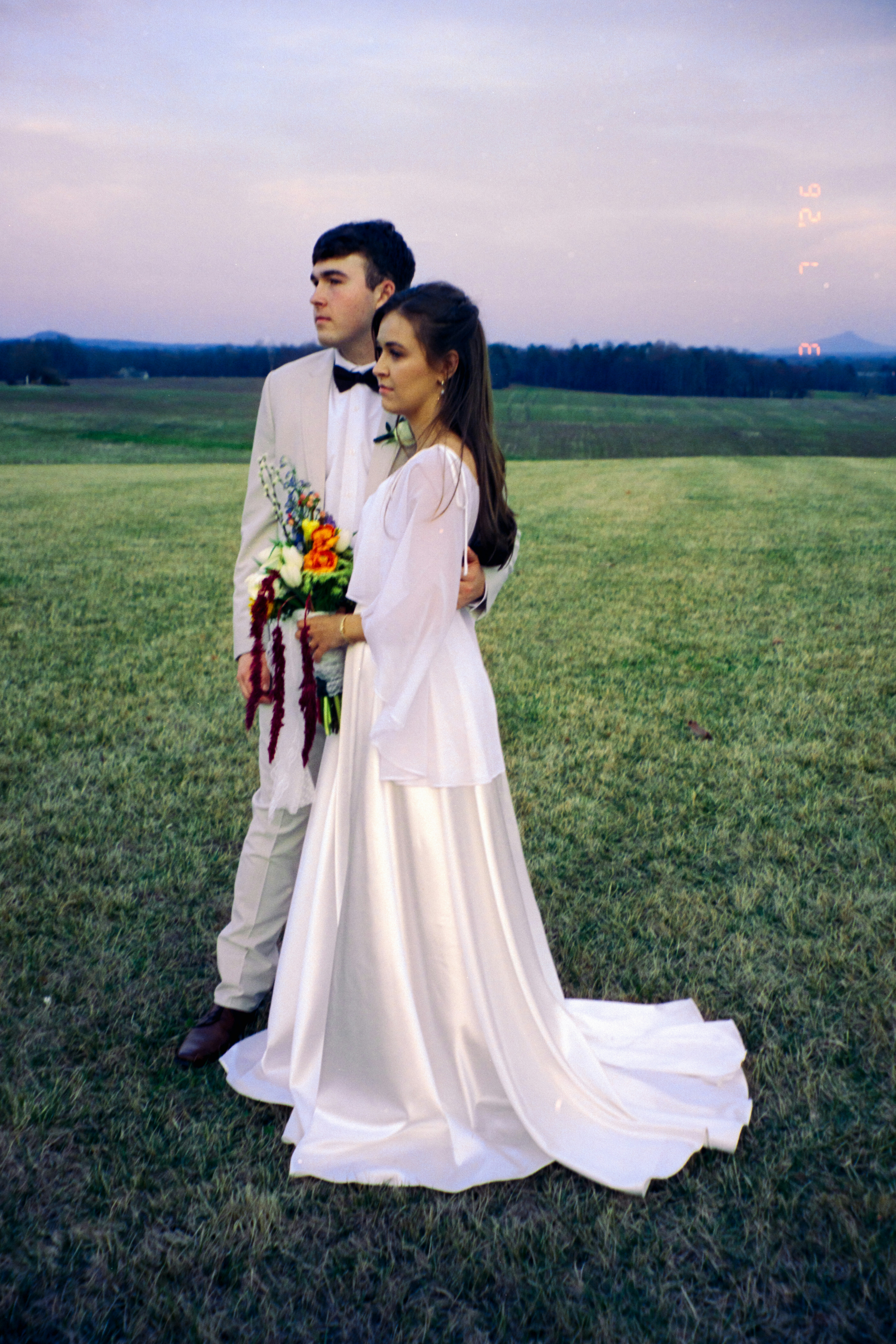 Um casal de noivos parado em um campo gramado.