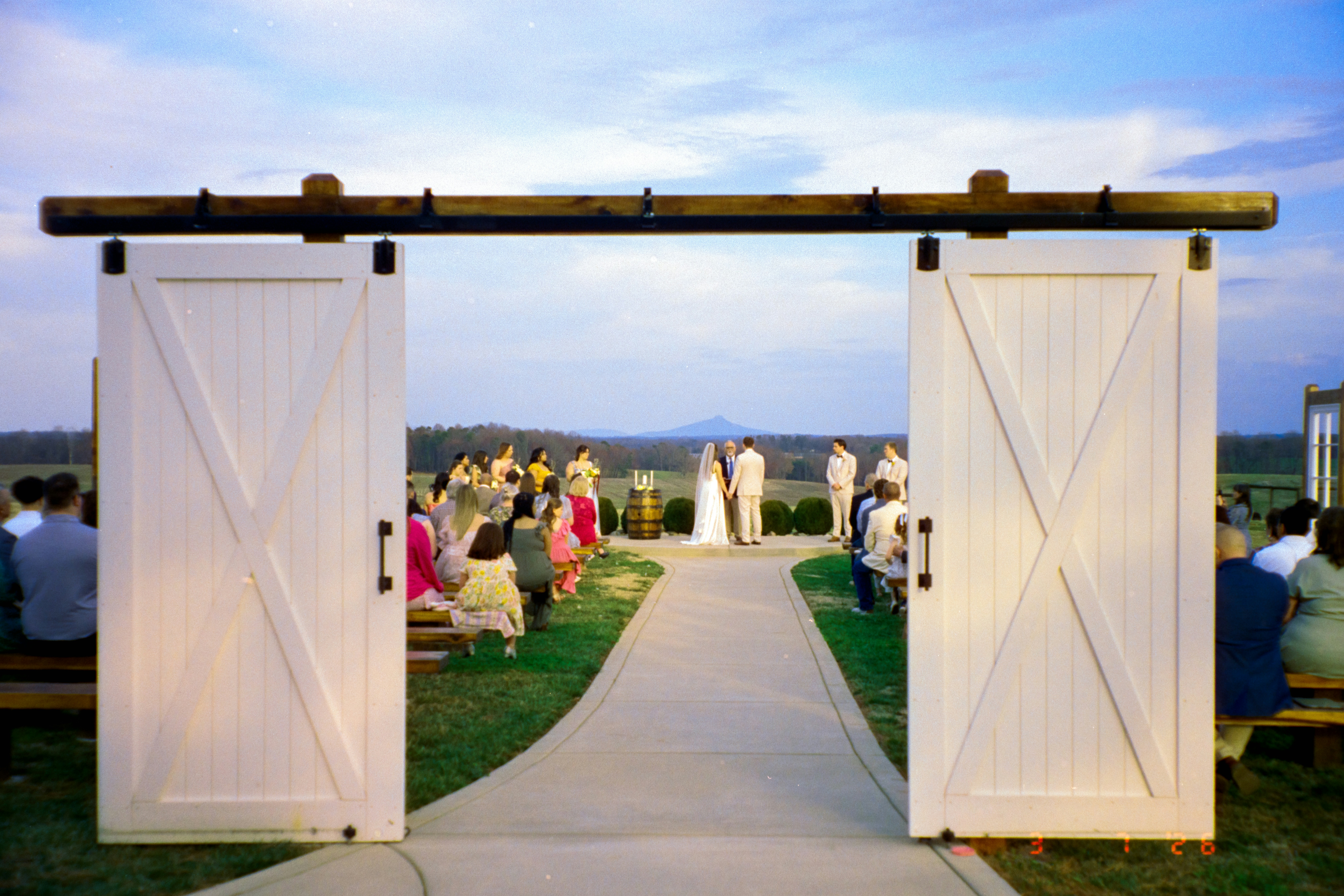 Cerimônia de casamento com portas abertas no celeiro e convidados sentados.